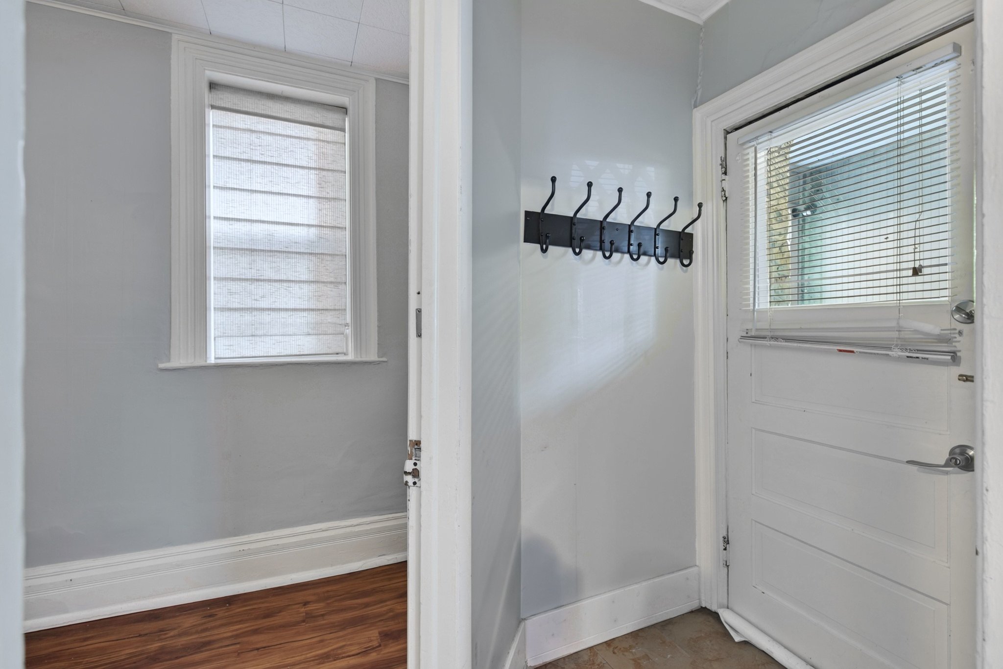 Entryway featuring a white paneled door with integrated blinds, a wall-mounted coat rack, light gray walls, and white trim