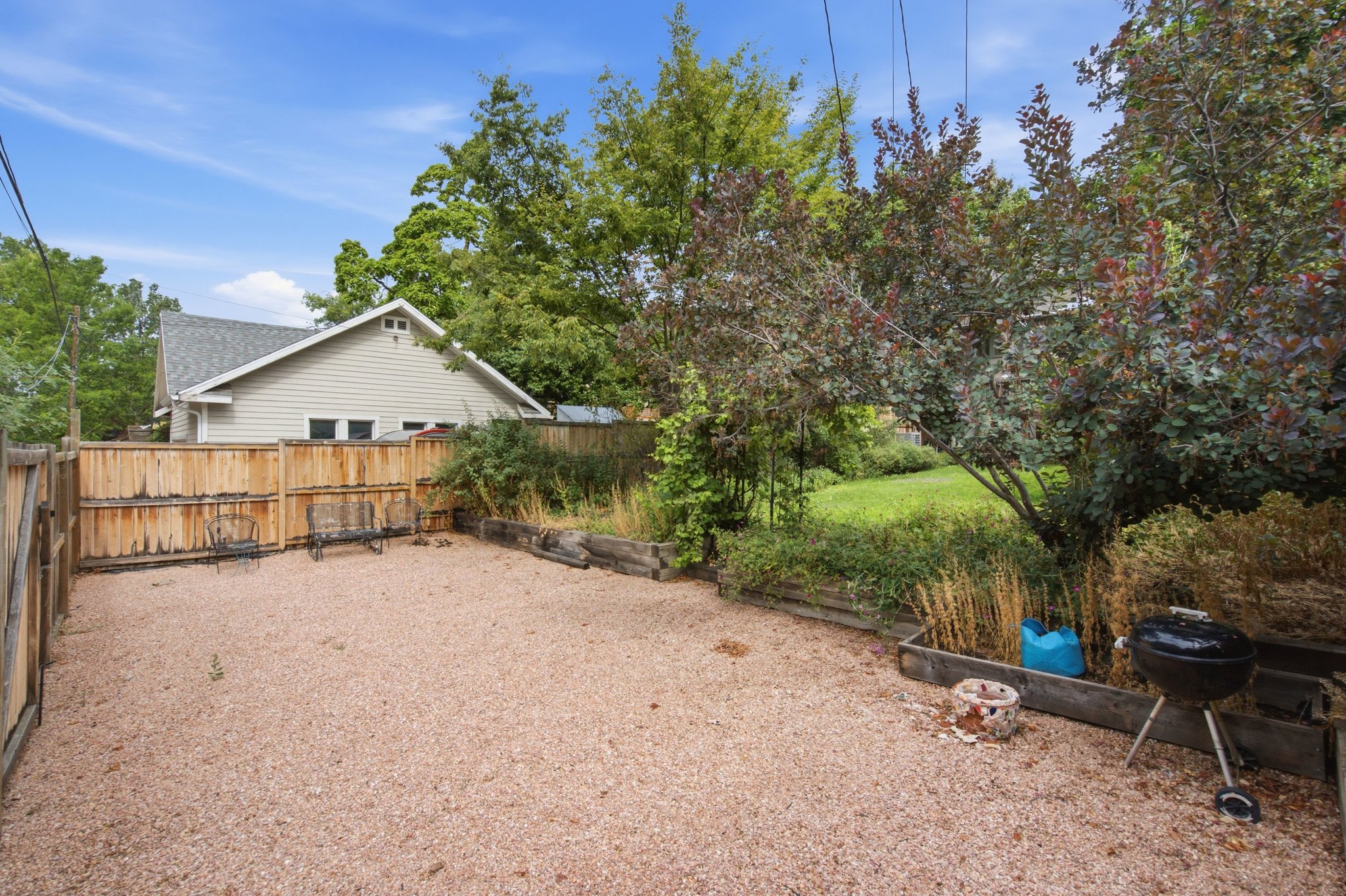 Gravel-covered outdoor area with wood fencing and mature trees