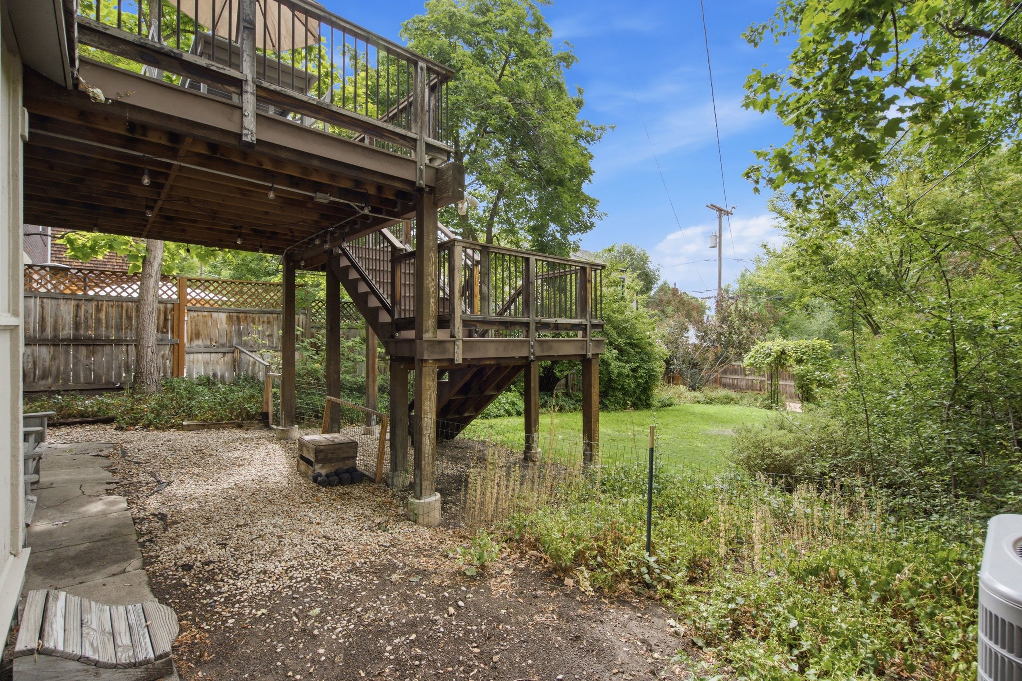 Multi-level wood deck featuring railings and stairs, overlooking a gravel patio and a grassy yard