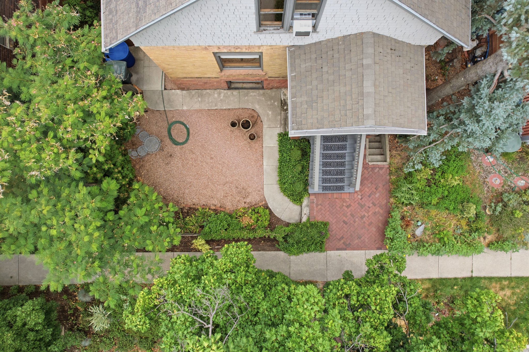 Aerial perspective showcasing a property with a gabled roof, a covered entry porch, a red brick pathway, mature landscaping, and an adjacent concrete walkway
