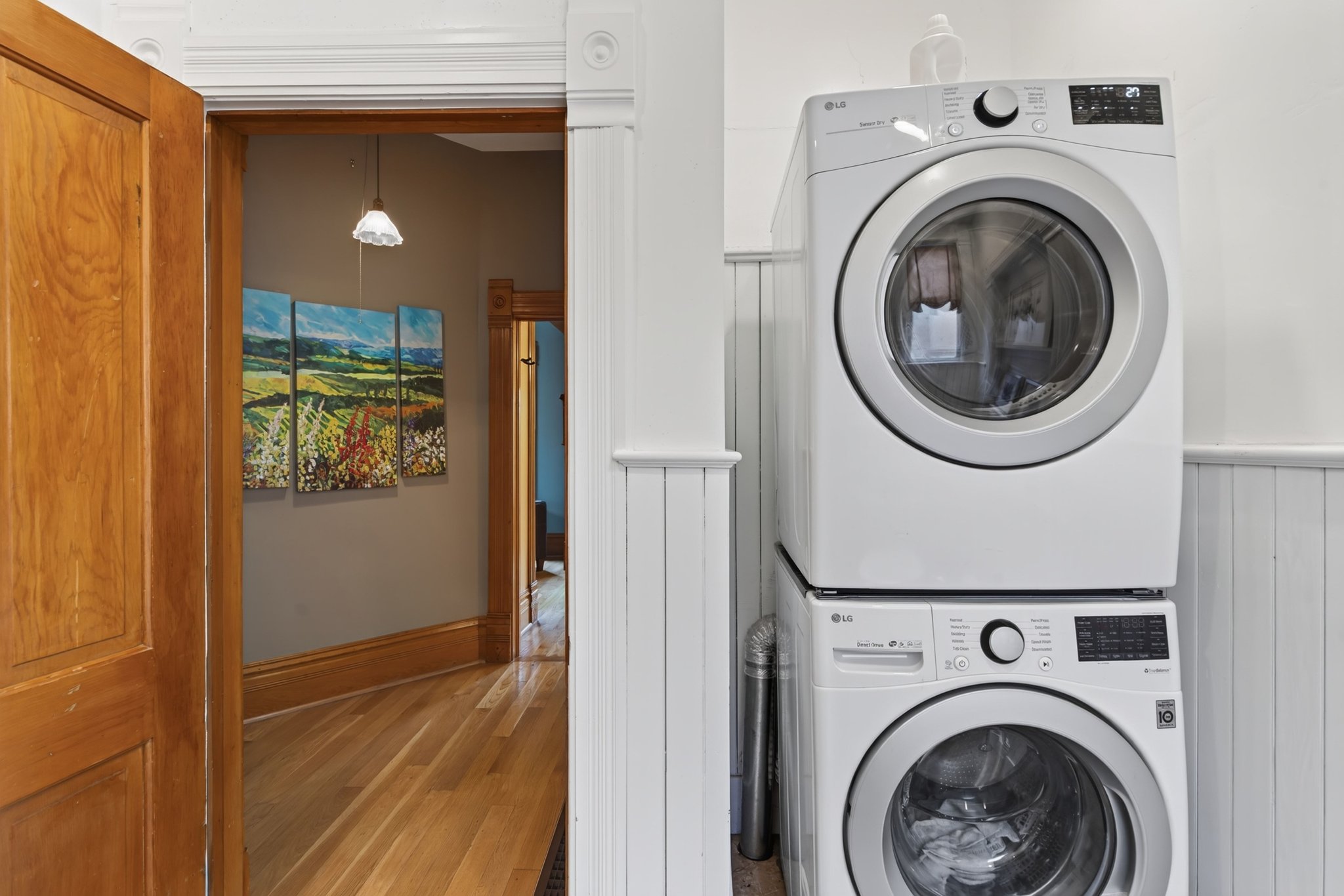 Stackable washer and dryer unit, white beadboard paneling, light wood-finish flooring, and natural wood trim work