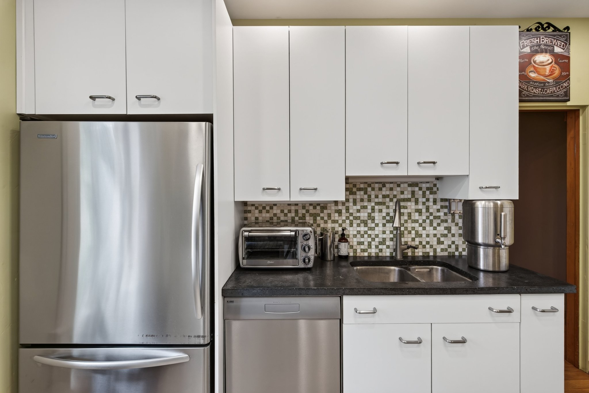 Contemporary kitchen featuring white cabinetry with silver-tone hardware, a stainless steel refrigerator, and a mosaic tile backsplash
