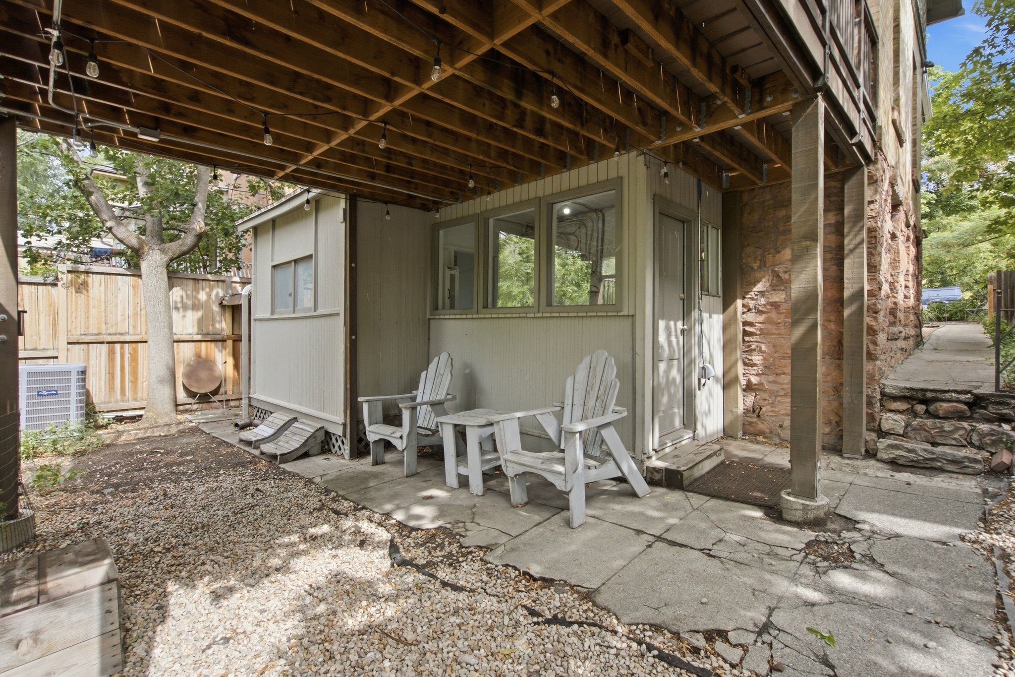 Covered outdoor patio area featuring string lights, concrete flooring, and a stone retaining wall