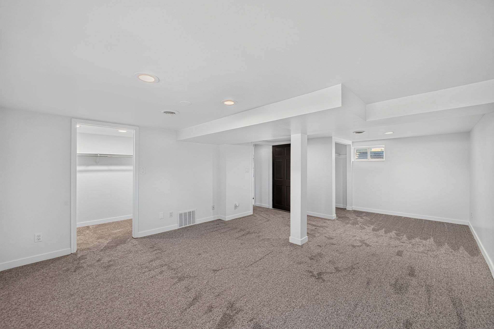 Spacious lower-level area with neutral carpeting, recessed ceiling lighting, a built-in closet with shelving, and a small window