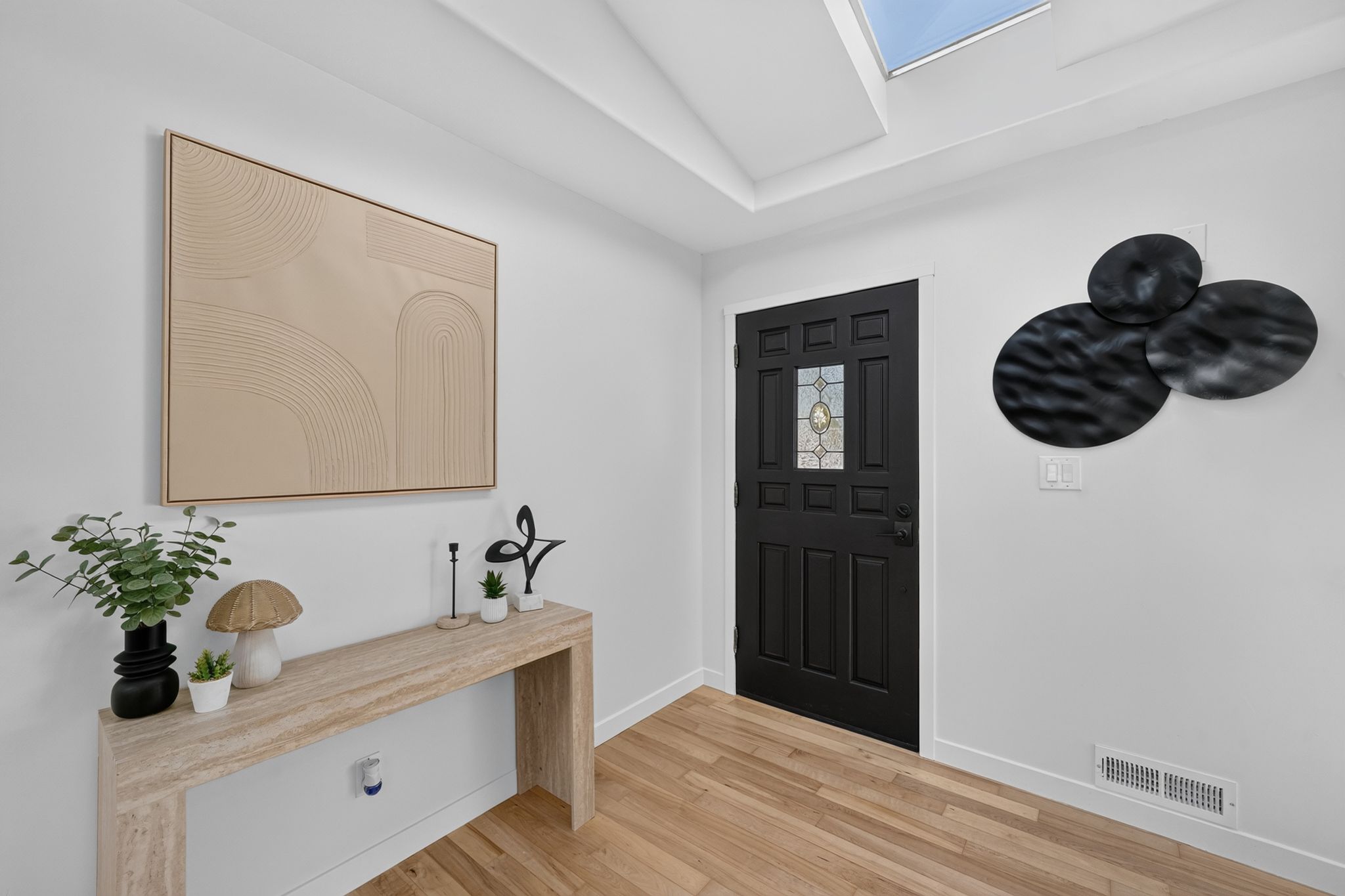 Entryway featuring a dark paneled door with a leaded glass insert, wood-finish flooring, a skylight, and white baseboards