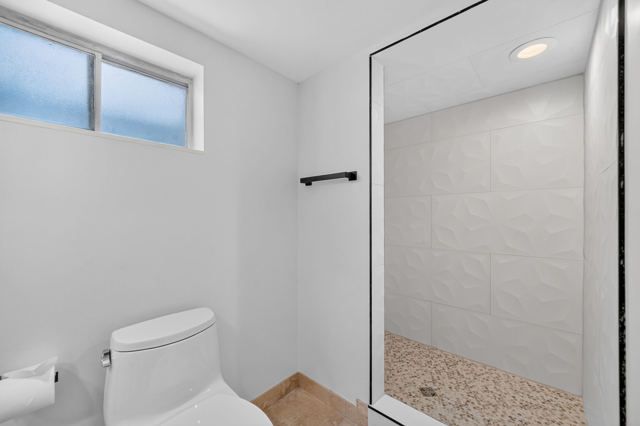 Walk-in shower featuring textured white tile walls and a pebble-finish floor