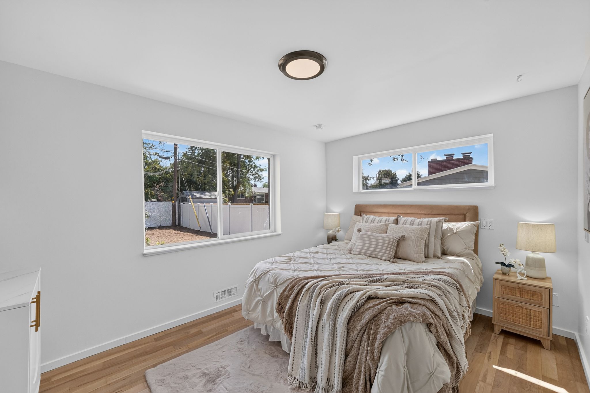 Bedroom with wood-finish flooring, white walls, two distinct windows, and a flush-mount ceiling light fixture