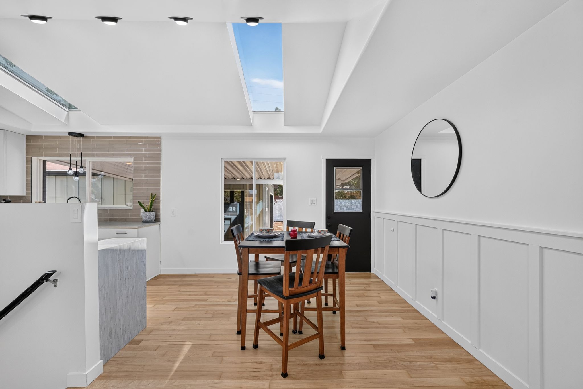 Open-concept living space with a large skylight, wood-finish flooring, and white paneling