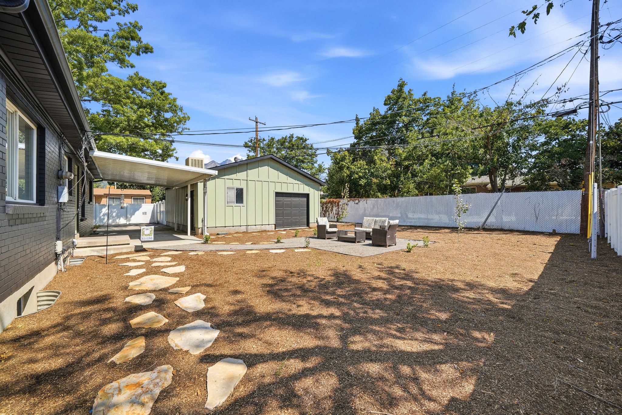 Expansive backyard featuring a large paved patio, a stone pathway, and a detached garage with a dark-finish door
