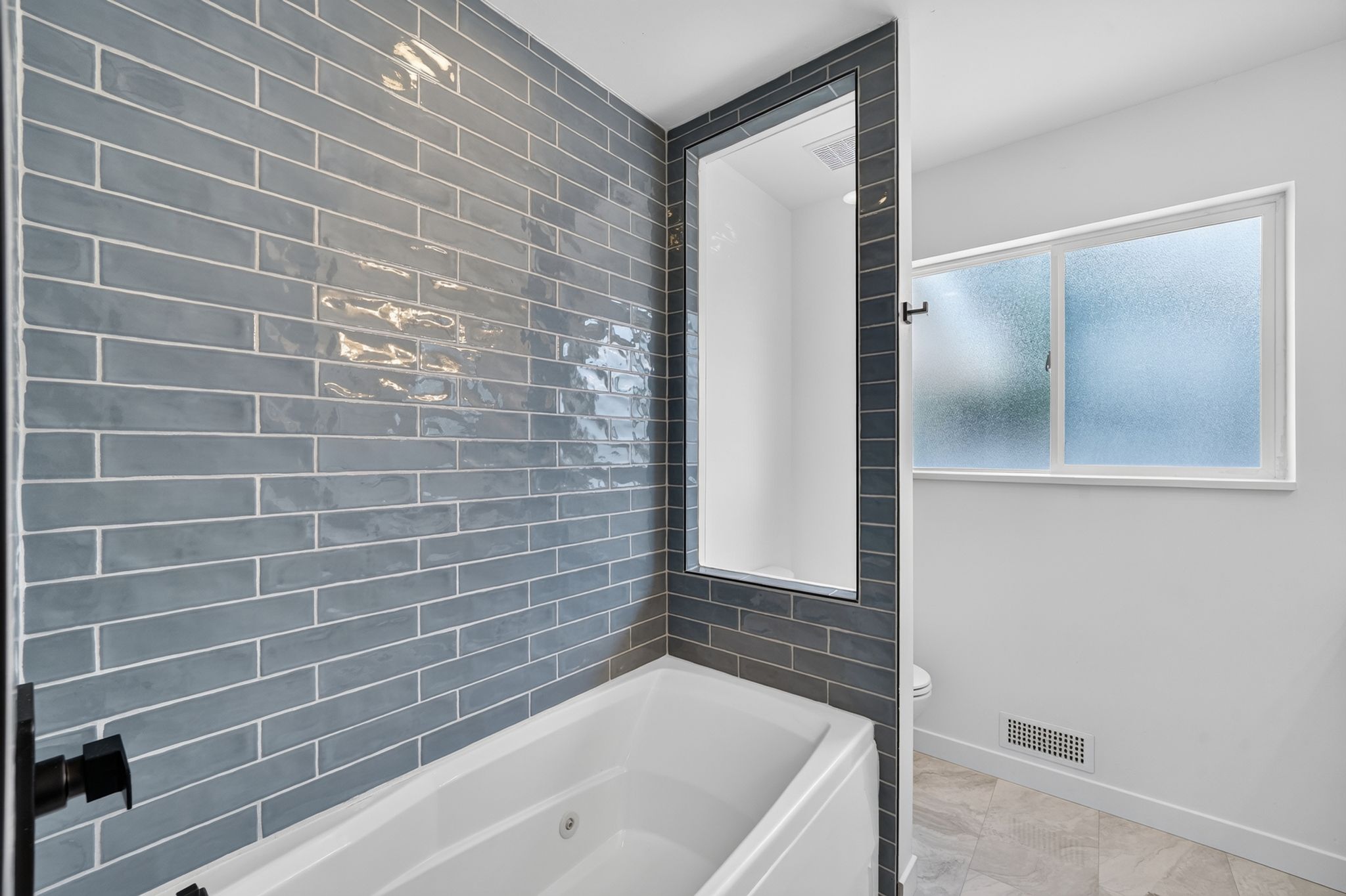 Bathroom featuring a built-in bathtub with matte black fixtures, full-height subway tile surround, and a frosted window