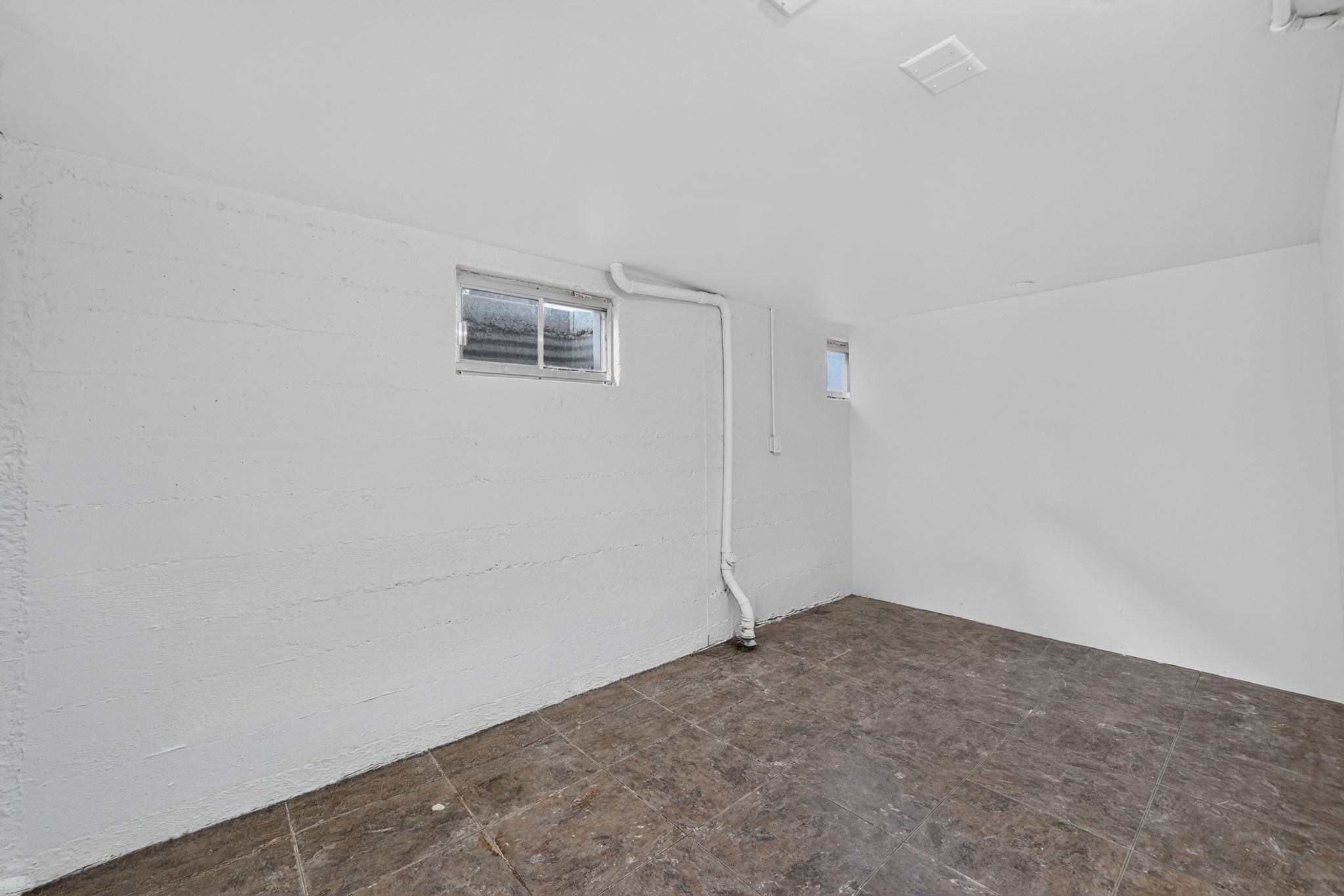 Spacious basement room featuring white-painted walls, a window providing natural light, and durable tile flooring