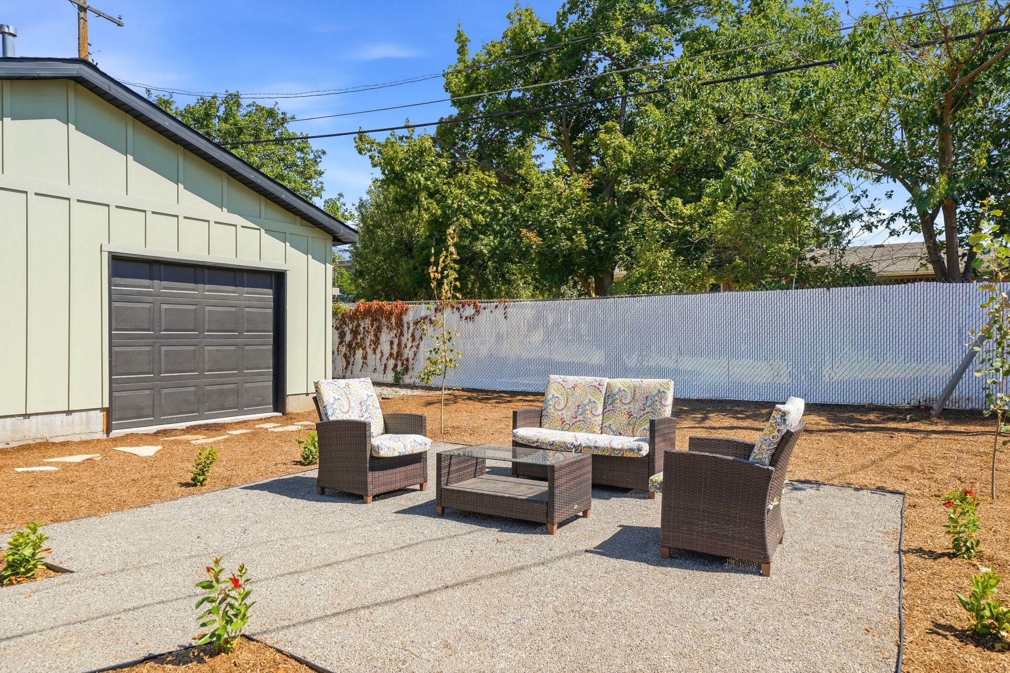 Spacious outdoor patio area featuring a gravel surface, surrounded by fresh mulch, with a white privacy fence