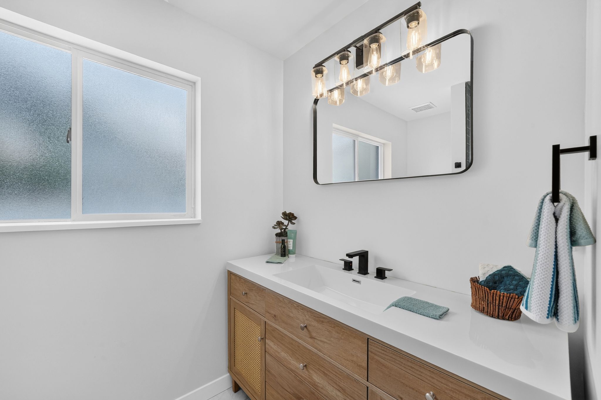 Modern bathroom featuring a wood-finish vanity with integrated sink, white countertop, and matte black fixtures