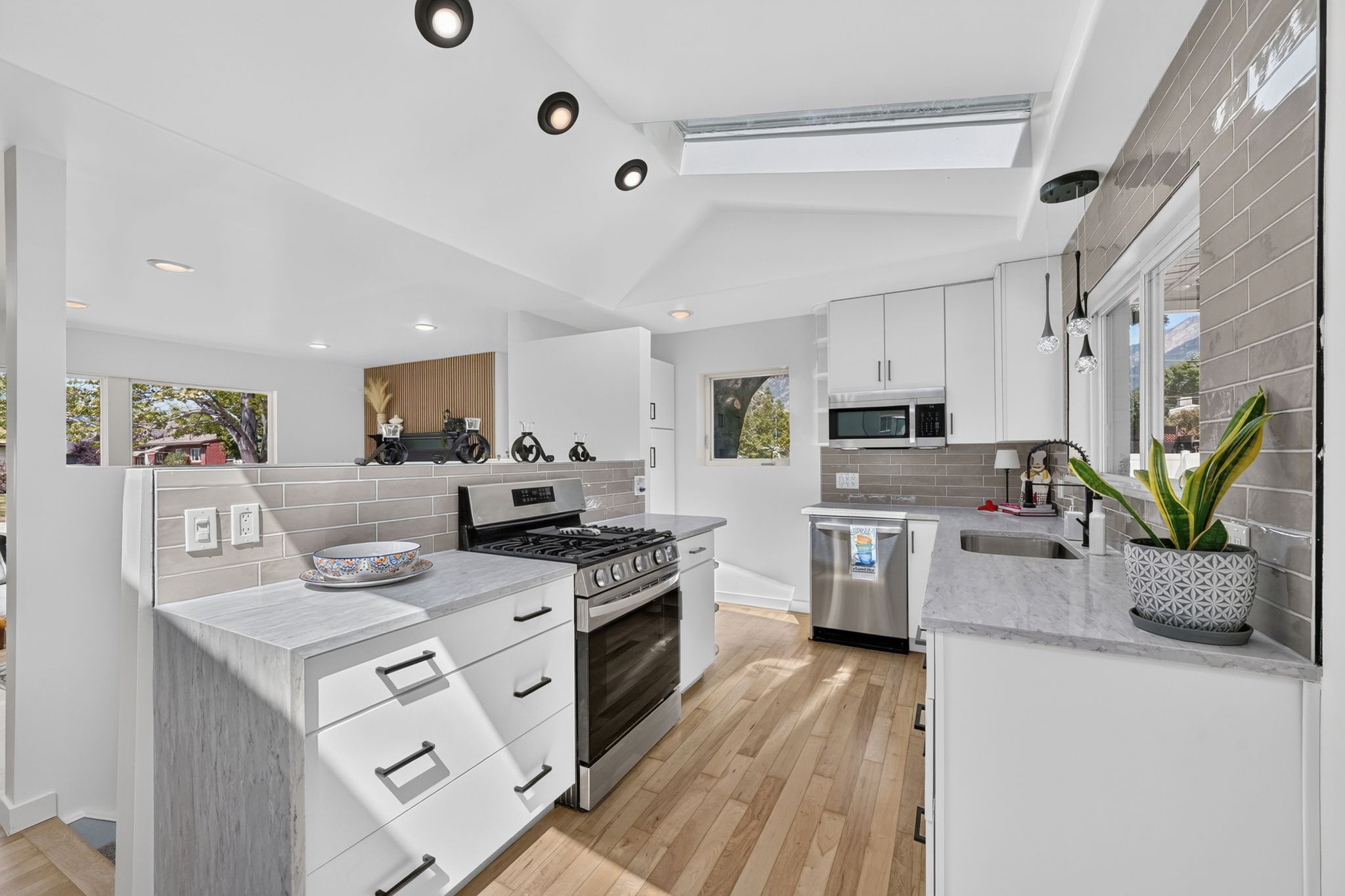 Modern kitchen featuring stainless steel appliances, light wood-finish flooring, white cabinetry, gray subway tile backsplash, and recessed lighting