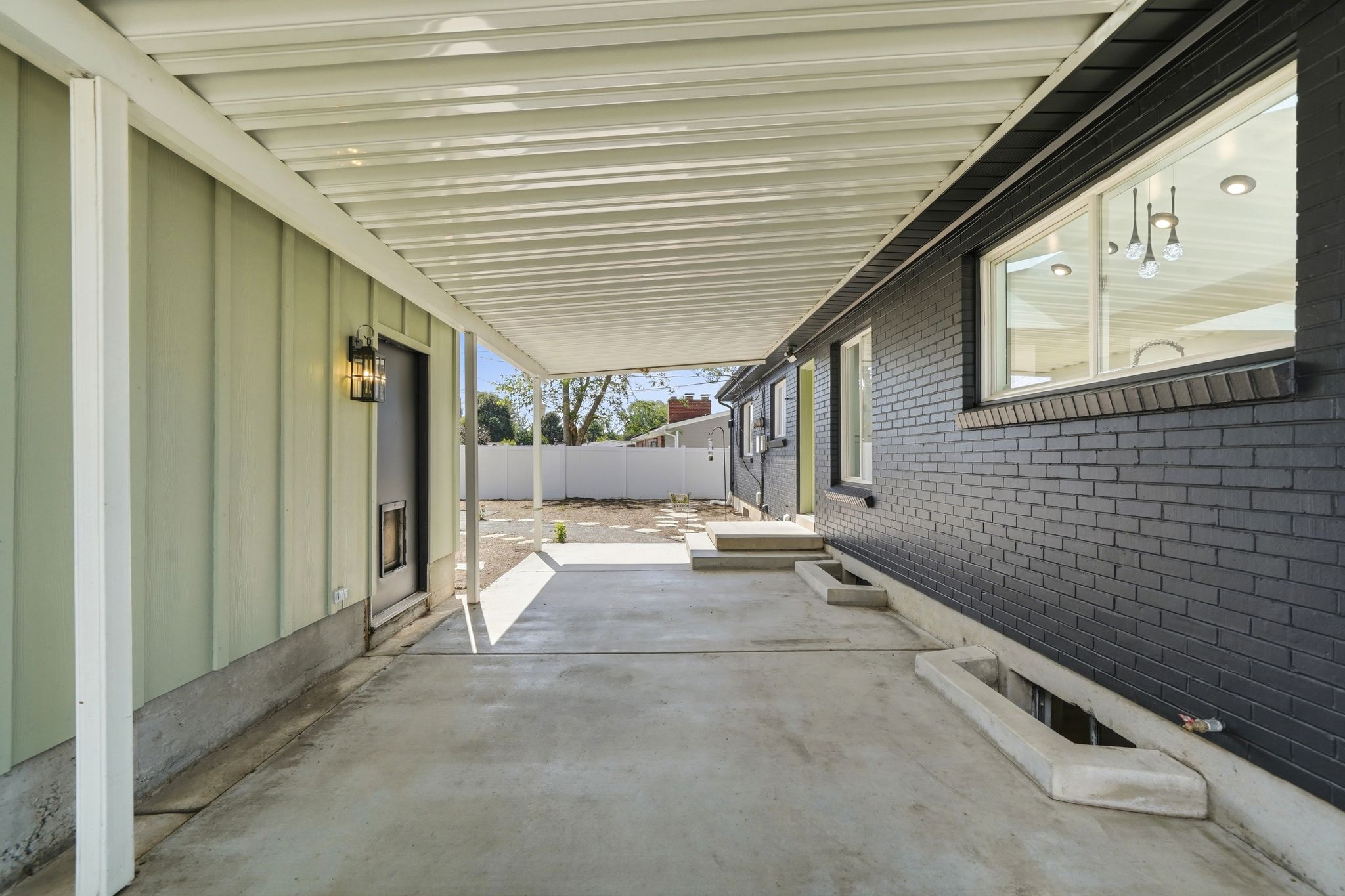 Covered patio area featuring a concrete surface, board and batten siding, dark brick exterior, exterior lighting fixture, and multiple windows