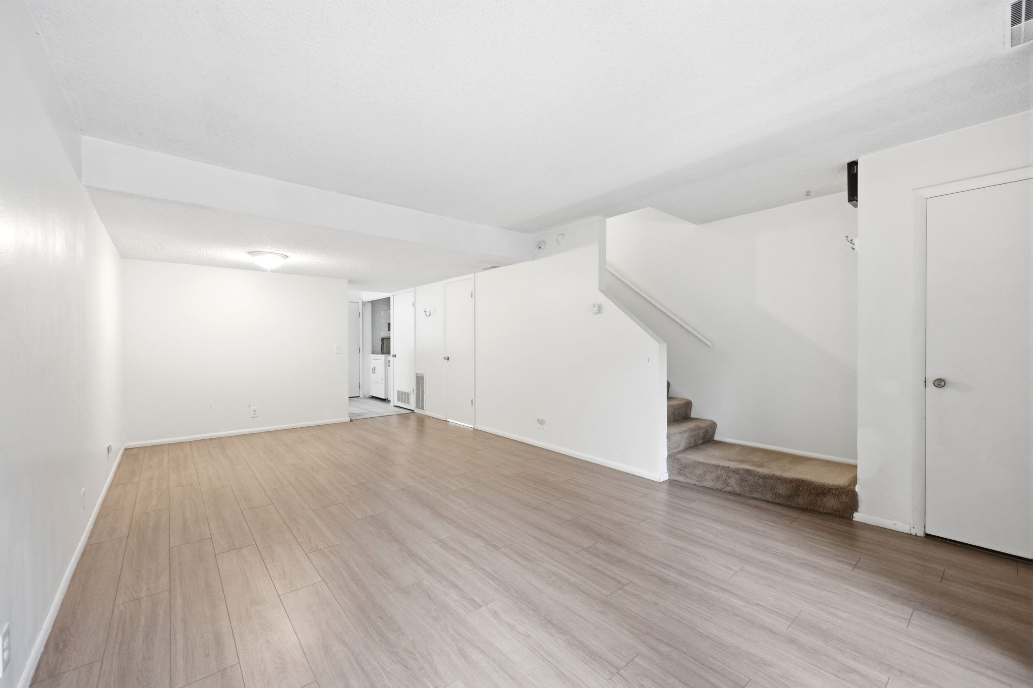 Spacious living area featuring wood-finish flooring, neutral white walls, and a ceiling light fixture