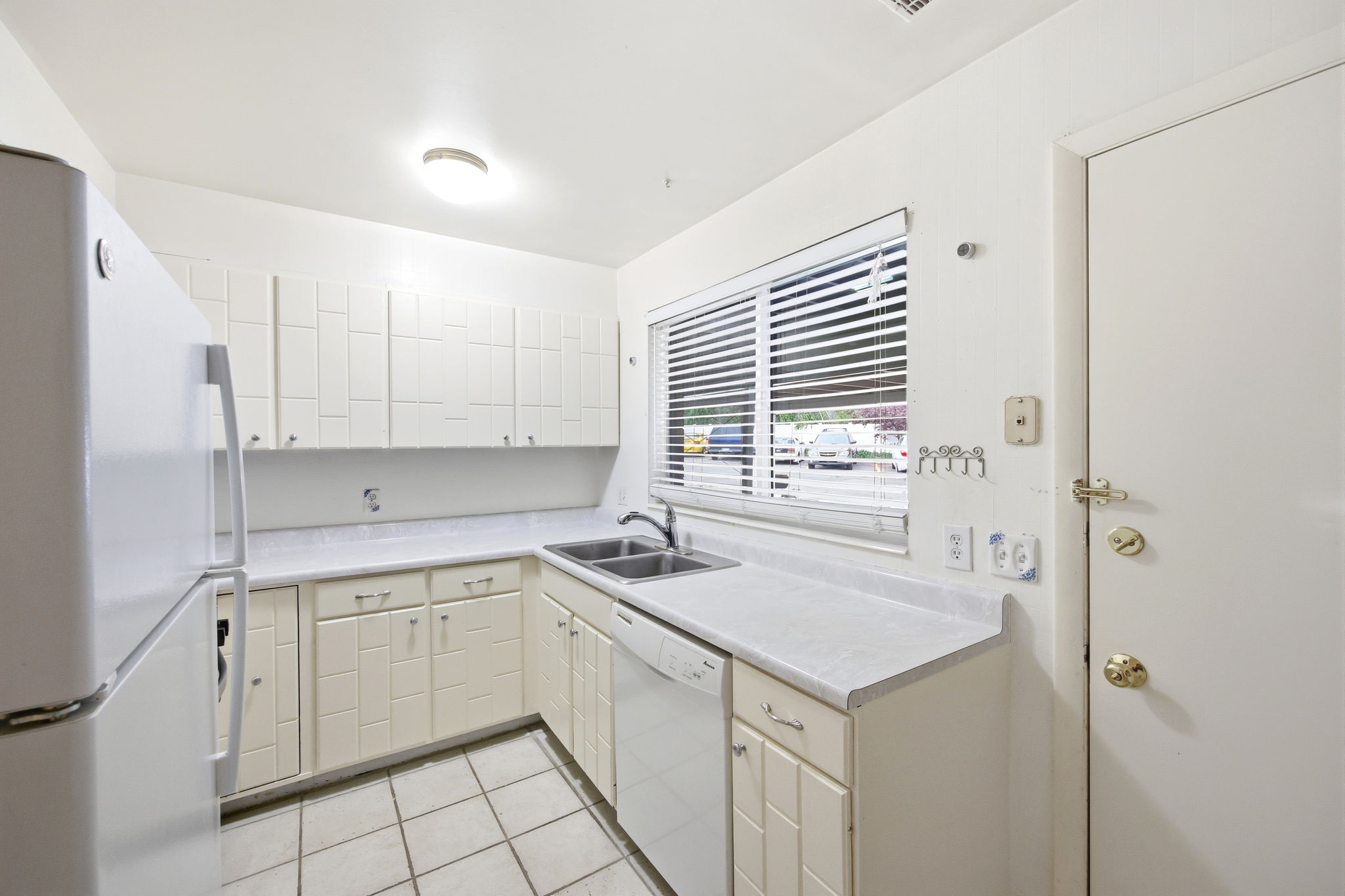 Kitchen featuring white tile flooring, white cabinetry, a double basin sink, white countertops, and a white dishwasher