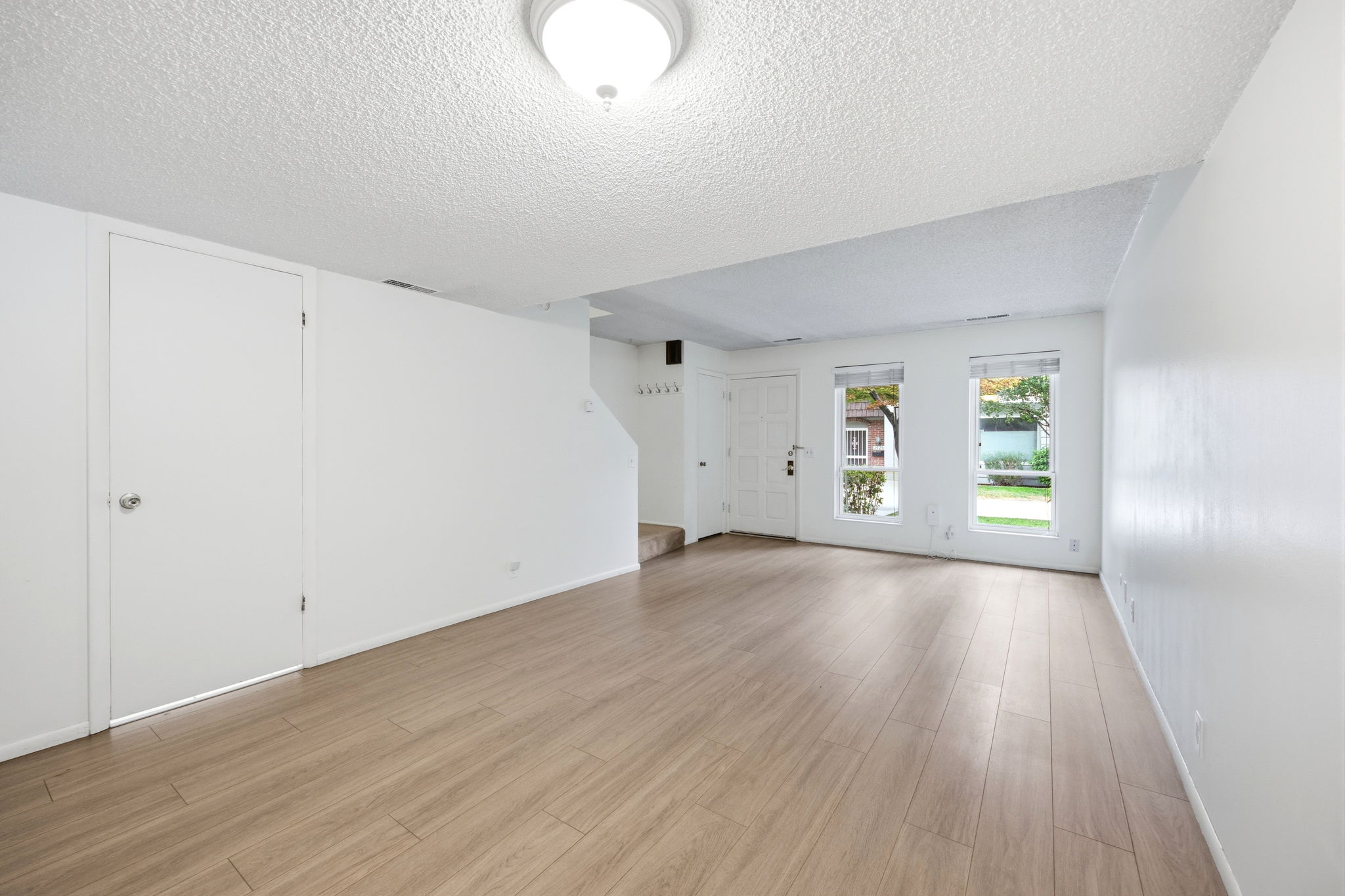 Spacious interior room featuring wood-finish flooring, white walls, and a textured ceiling