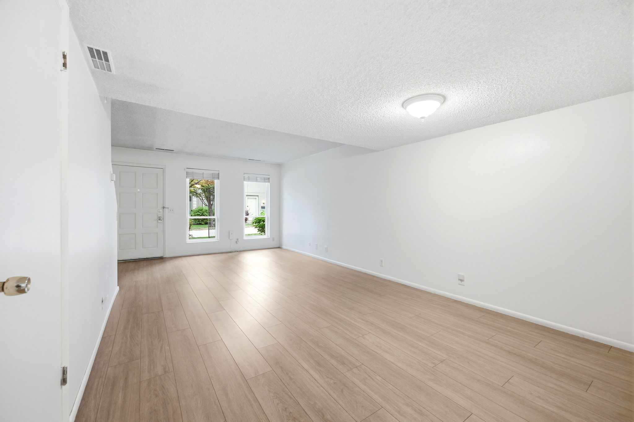 Spacious room featuring wood-finish flooring, white walls, and a bright ceiling light fixture