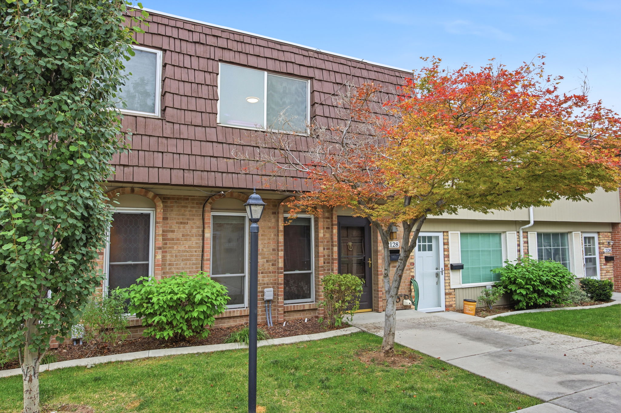 Townhome exterior featuring a brown shingle mansard roof, brick veneer lower level, and light-colored siding