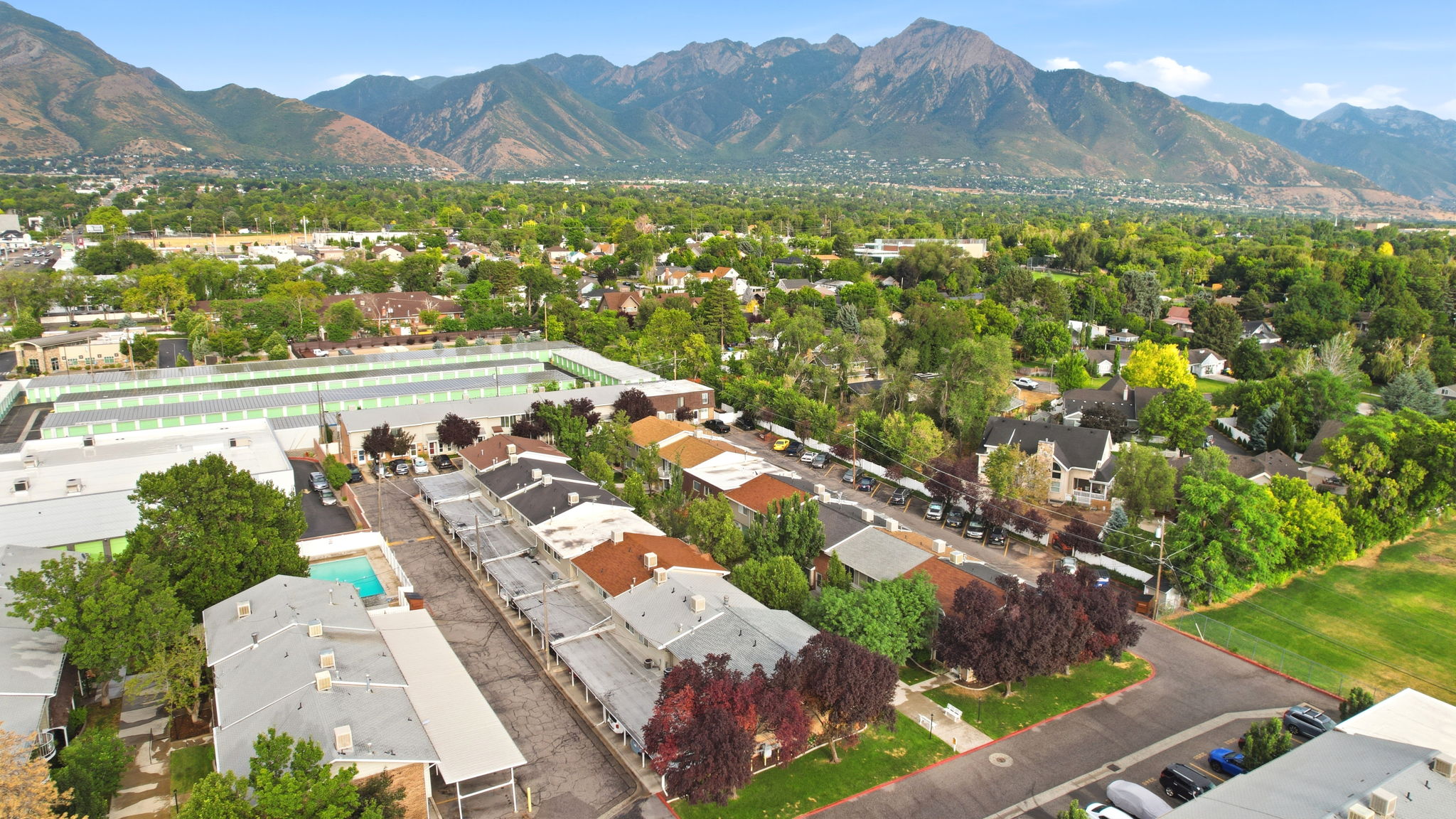 Aerial perspective showcasing a residential community with abundant green spaces, mature trees, and mountainous terrain in the background