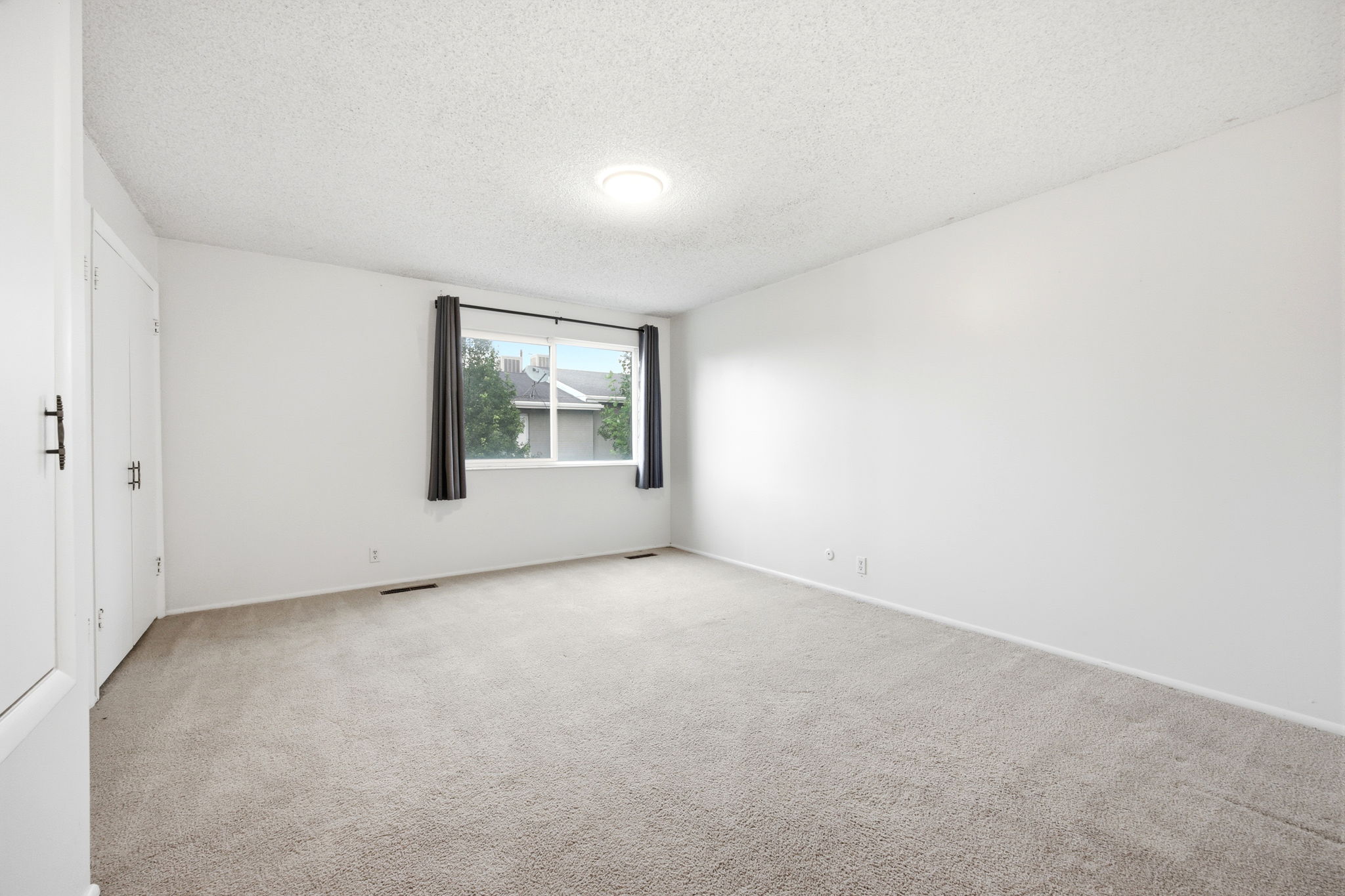 Carpeted room with a window featuring dark curtains, white walls, and brand new light fixture