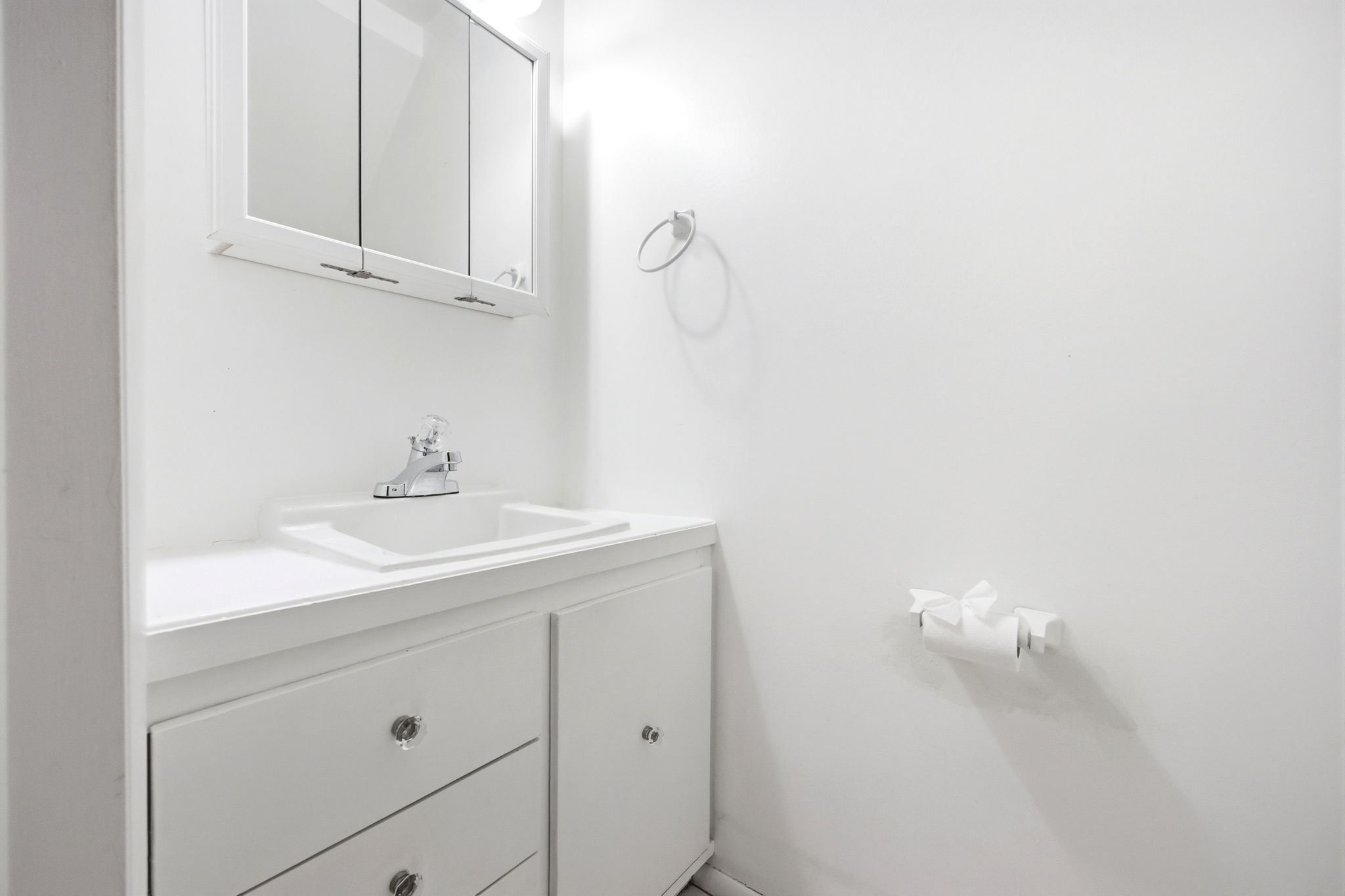 White vanity with an integrated sink, polished chrome faucet, and mirrored medicine cabinet