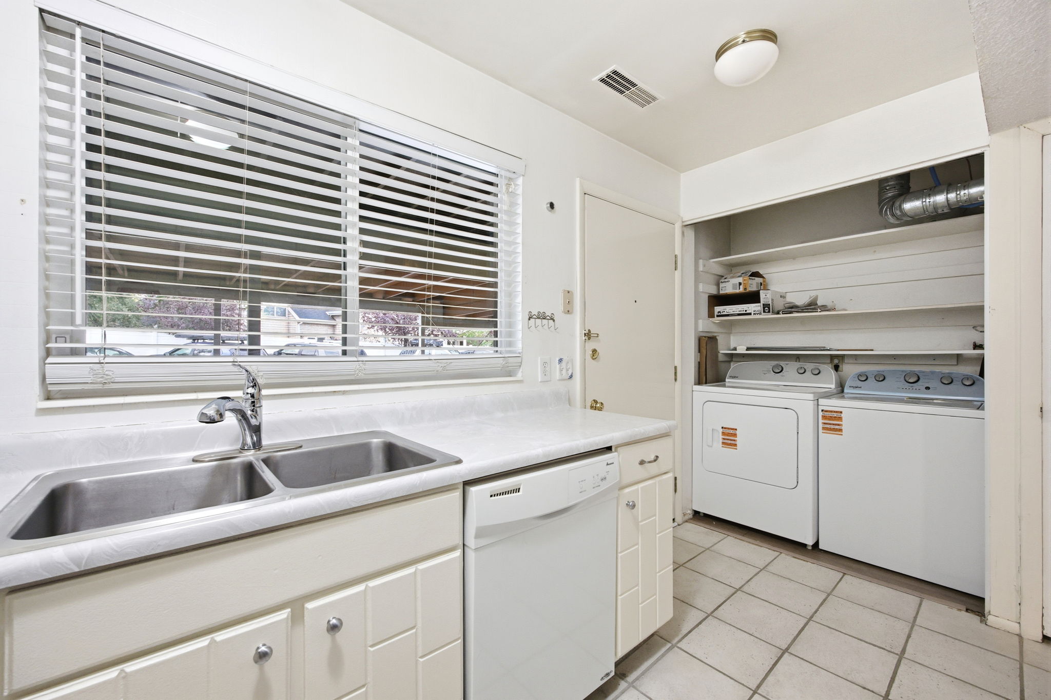 Kitchen area featuring a double basin stainless steel sink with a chrome faucet, light countertops, and white cabinetry