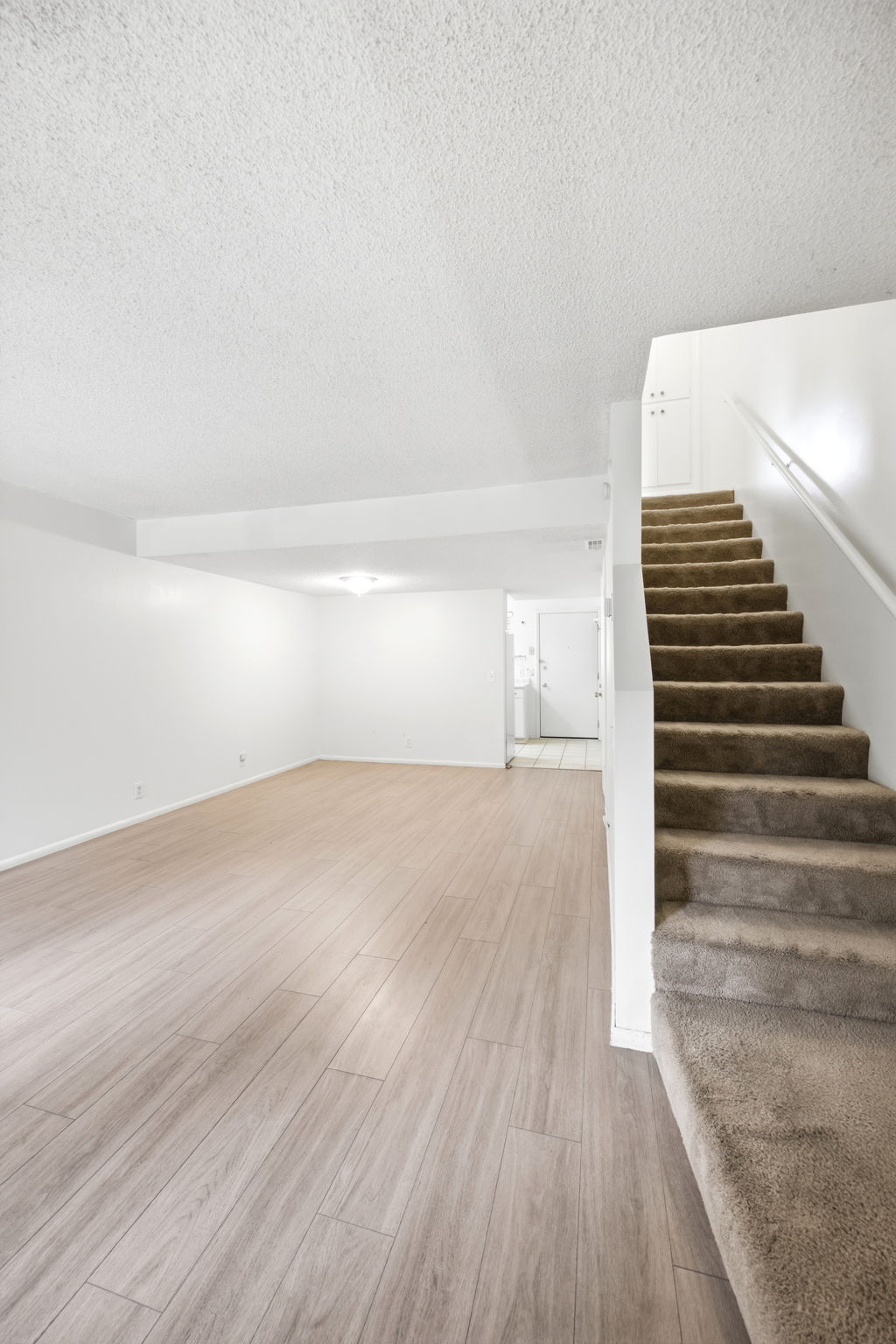 Spacious room with wood-finish flooring, white walls, and a newer bright light fixture