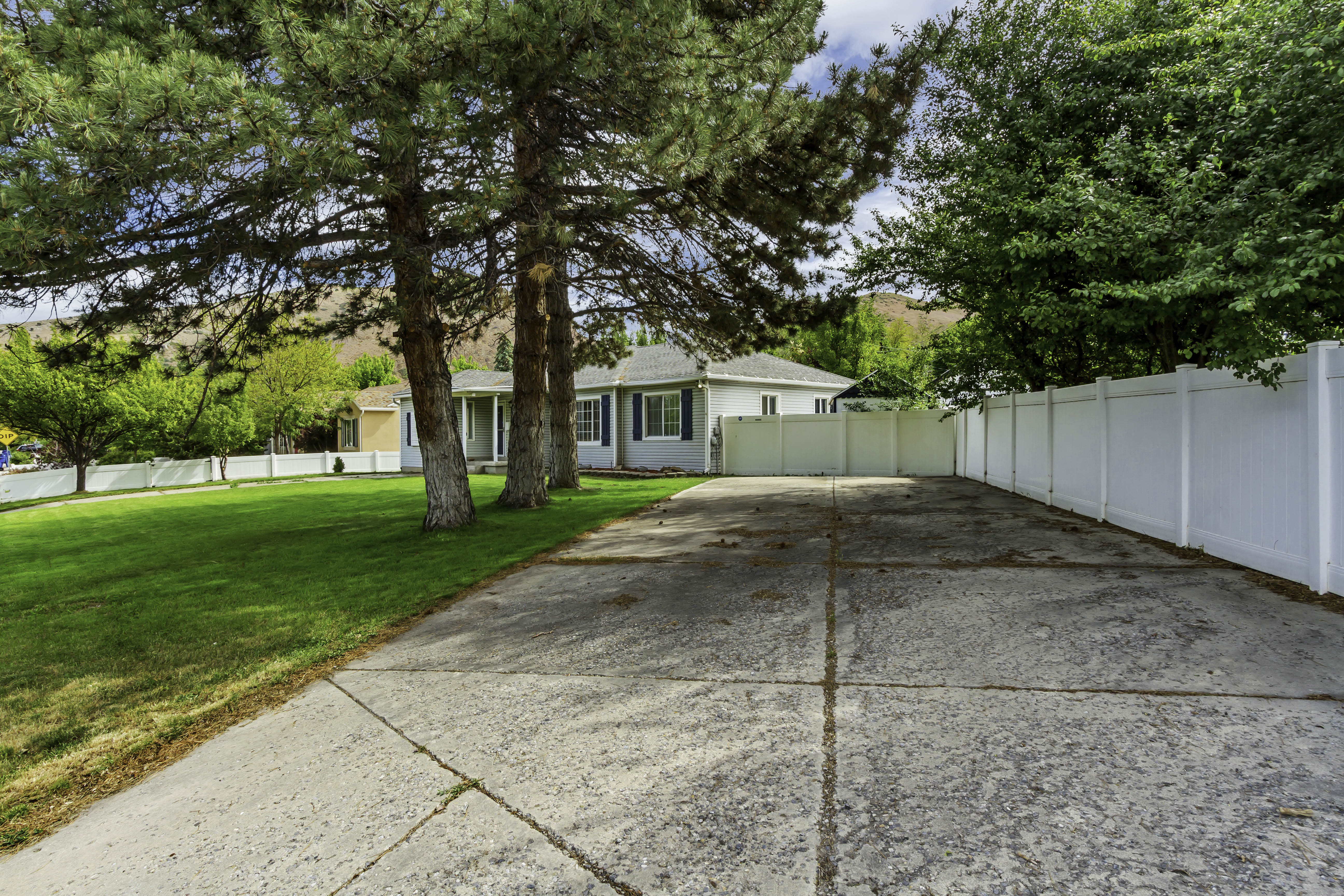 Expansive concrete driveway featuring a white vinyl privacy fence along one side