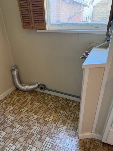 Utility area featuring patterned tile flooring, a window with wooden louvered shutters, and appliance hookups