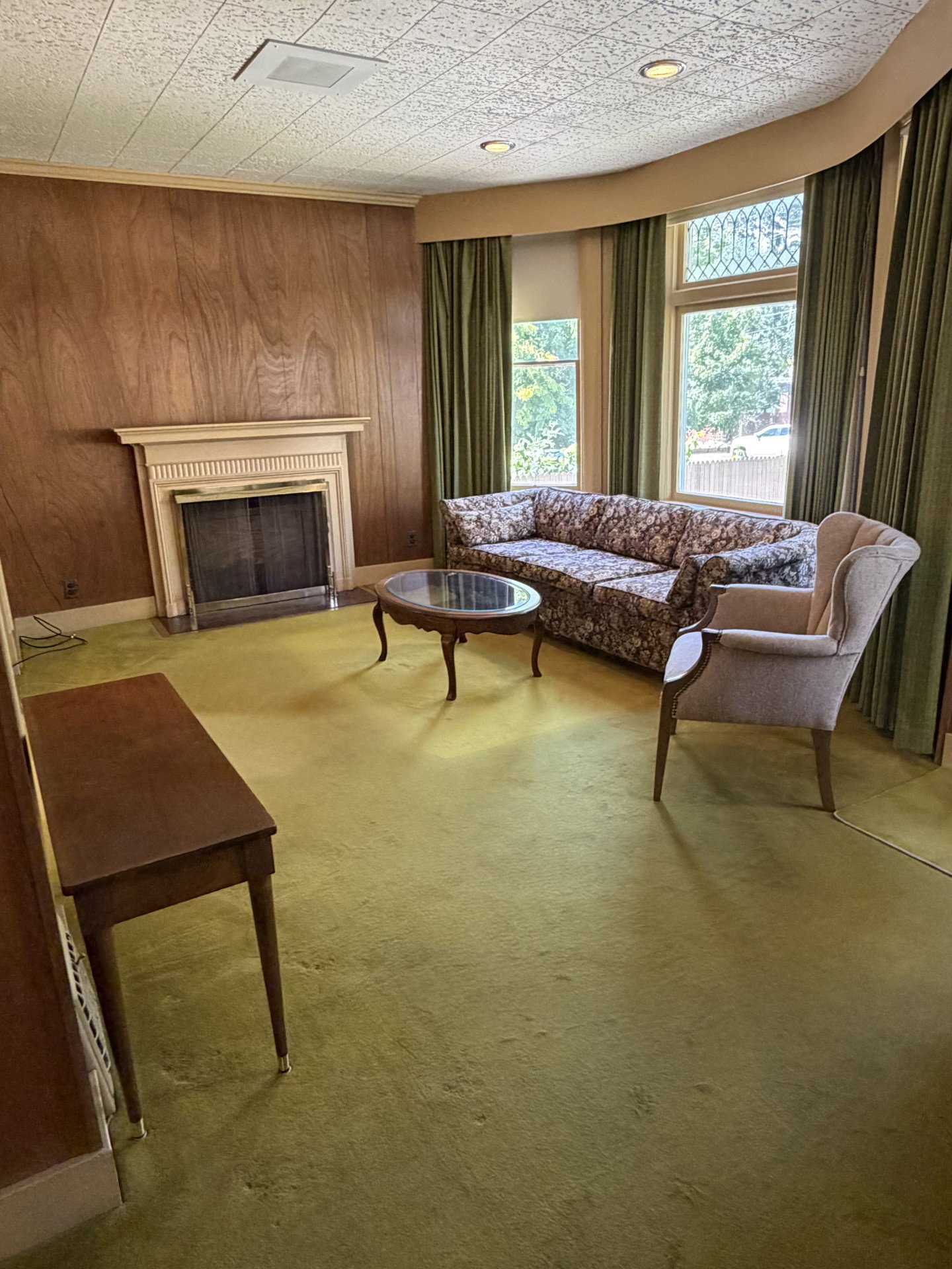 Living area featuring a fireplace with a mantel, wood-paneled accent wall, and a bay window with decorative glass