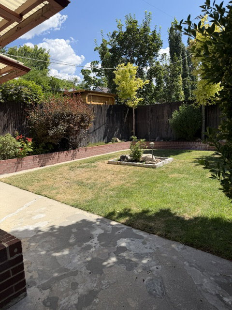 Expansive outdoor space featuring a concrete patio, brick garden borders, and a varied privacy fence