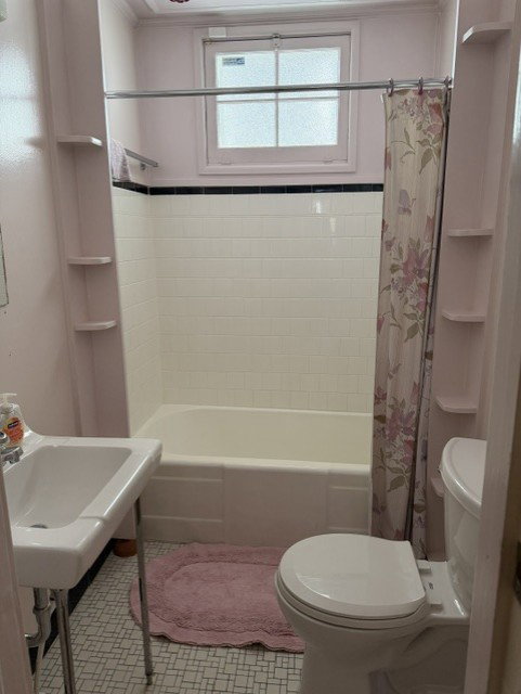 Bathroom with a white tile tub surround featuring a black accent border, a single window, and built-in shelving
