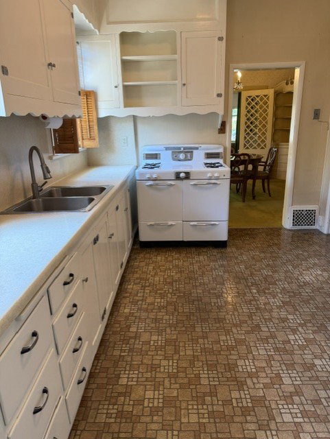Old style charm kitchen featuring extensive white cabinetry, a double basin stainless steel sink with a gooseneck faucet, light-toned countertops, and mosaic-patterned flooring