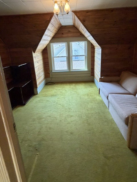 Office space featuring wood-panel walls, a vaulted ceiling, and dual windows with natural light.