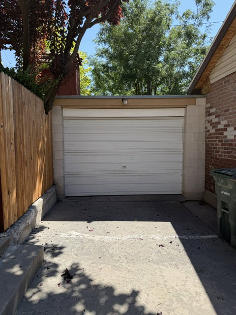 Detached garage featuring a white roll-up door, concrete block construction, and a newly installed wood privacy fence