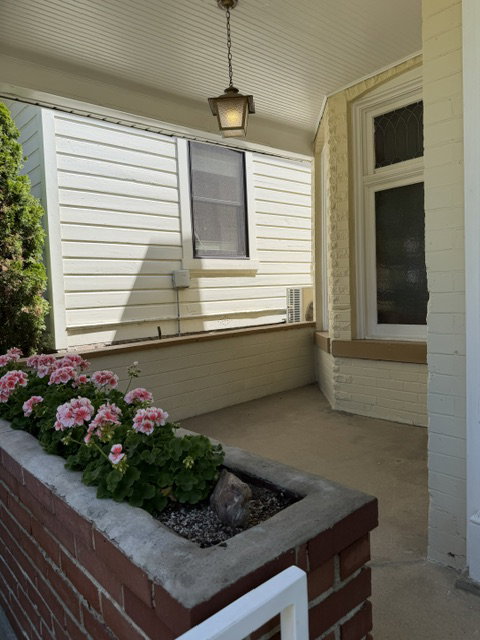 Covered porch featuring a brick planter, concrete flooring, and a decorative hanging light fixture