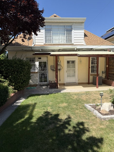 Rear exterior featuring a covered patio, two entry doors with security grilles, and an upper-level window bank