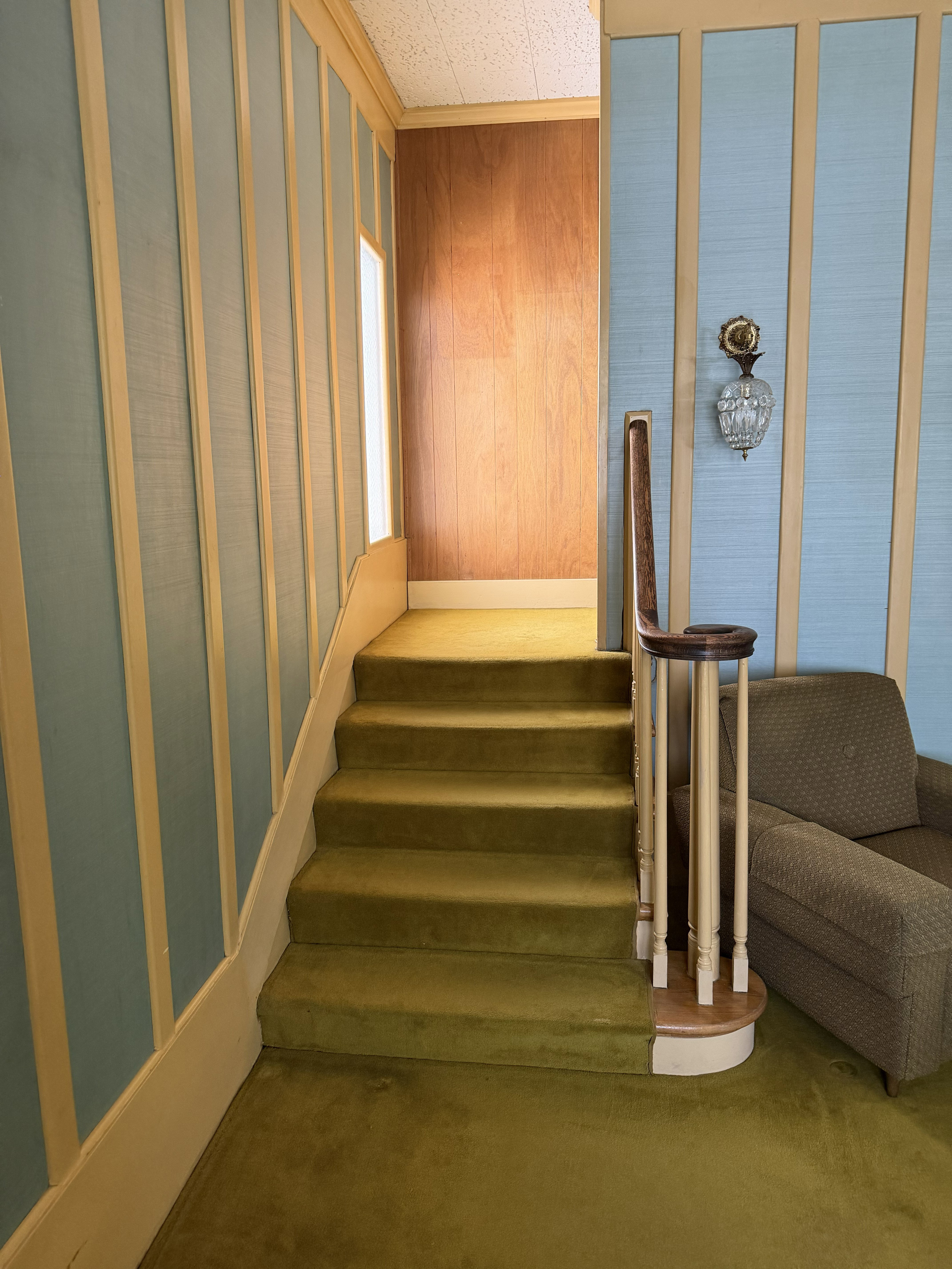 Carpeted staircase featuring a wooden handrail and balusters, framed by textured light blue wall panels with light-toned vertical trim