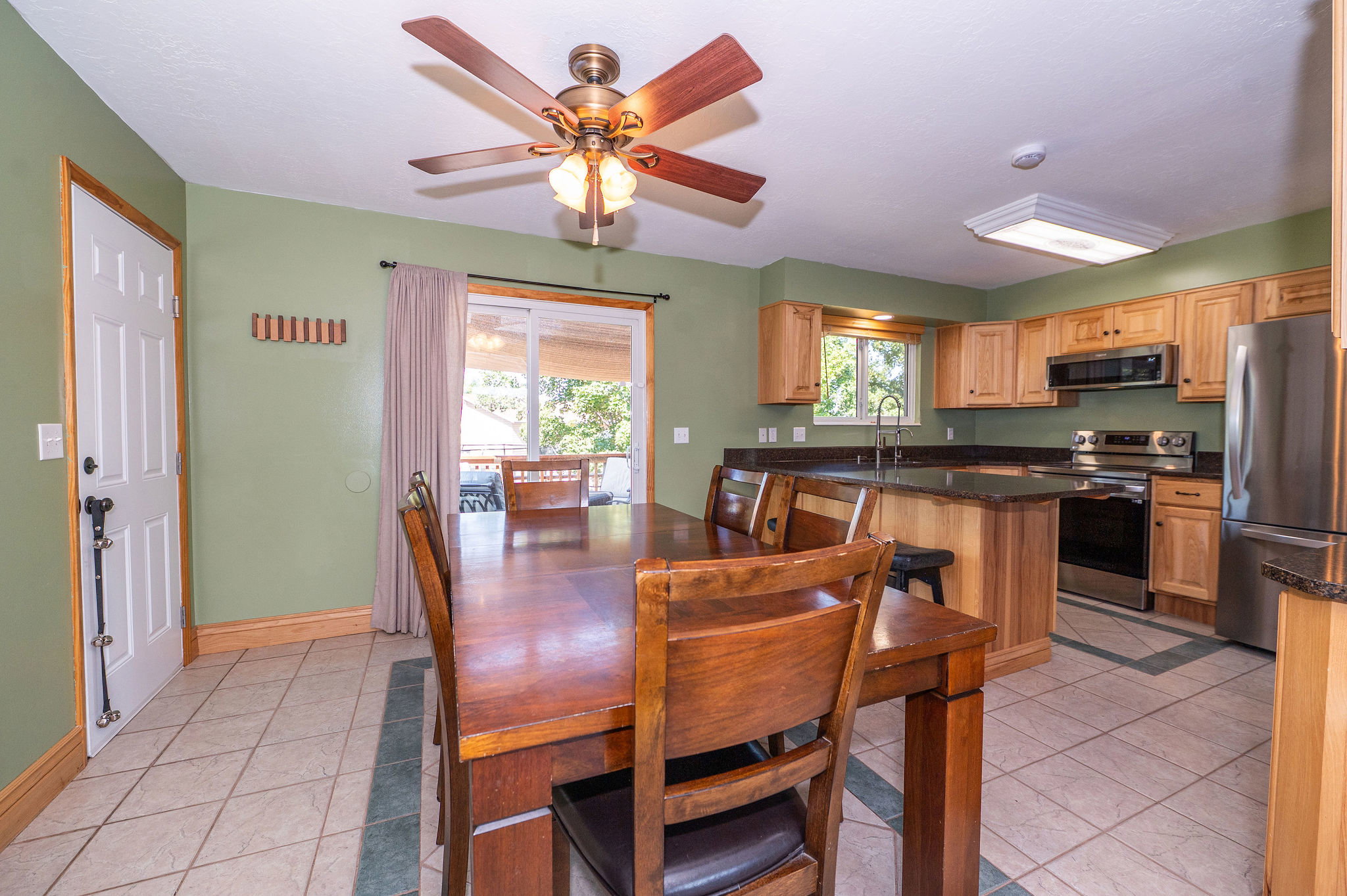 Kitchen and dining area featuring a ceiling fan, sliding glass door, tile flooring, wood cabinetry, and stainless steel appliances