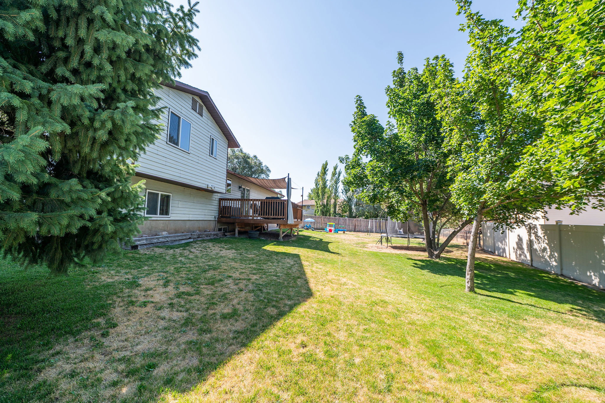 Expansive backyard featuring a wood deck with railing, mature trees, and a privacy fence along the perimeter