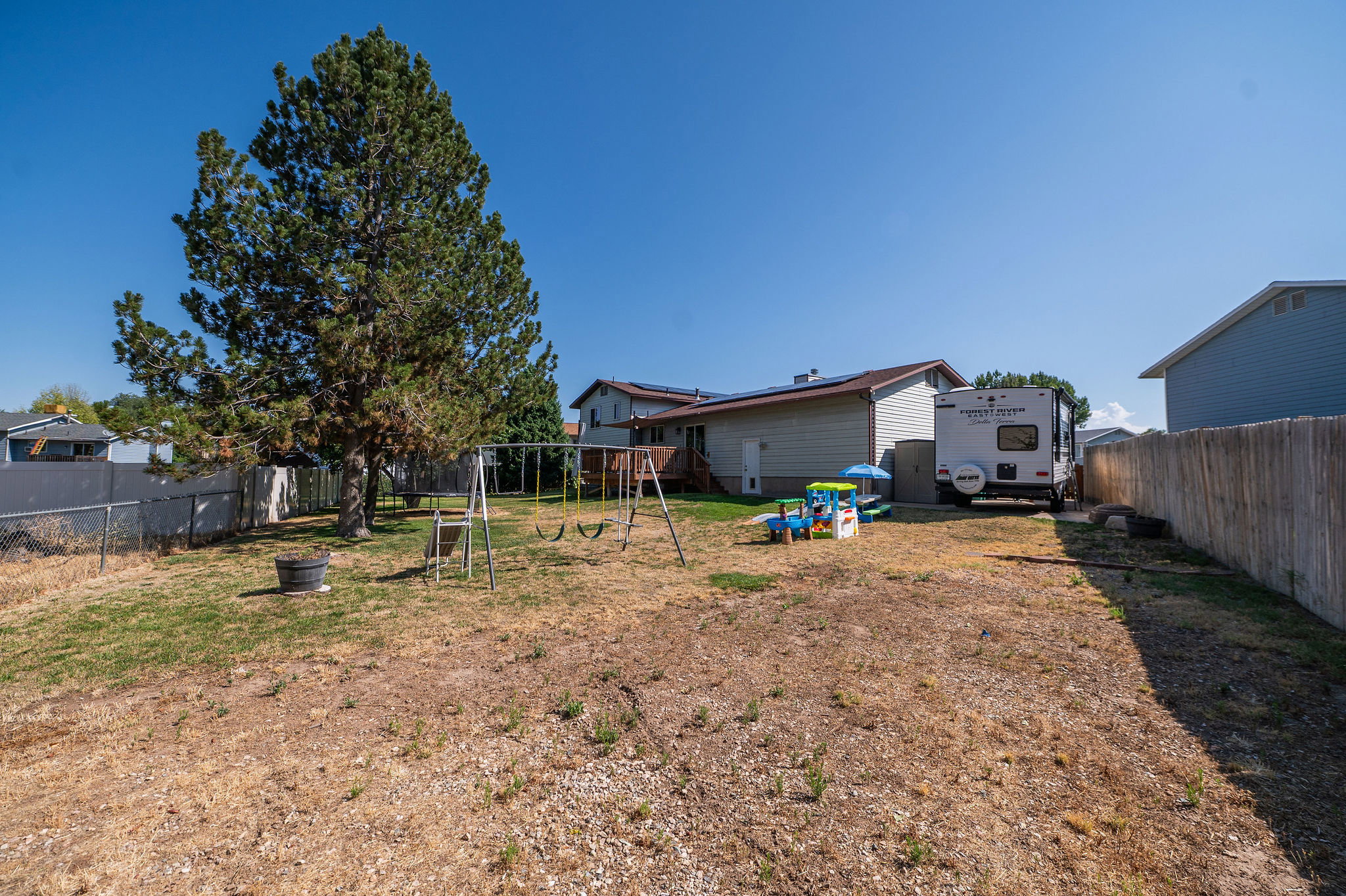 Expansive backyard featuring a mature evergreen tree, partially fenced perimeter with wood and chain-link fencing, and a gravel area extending along the right side