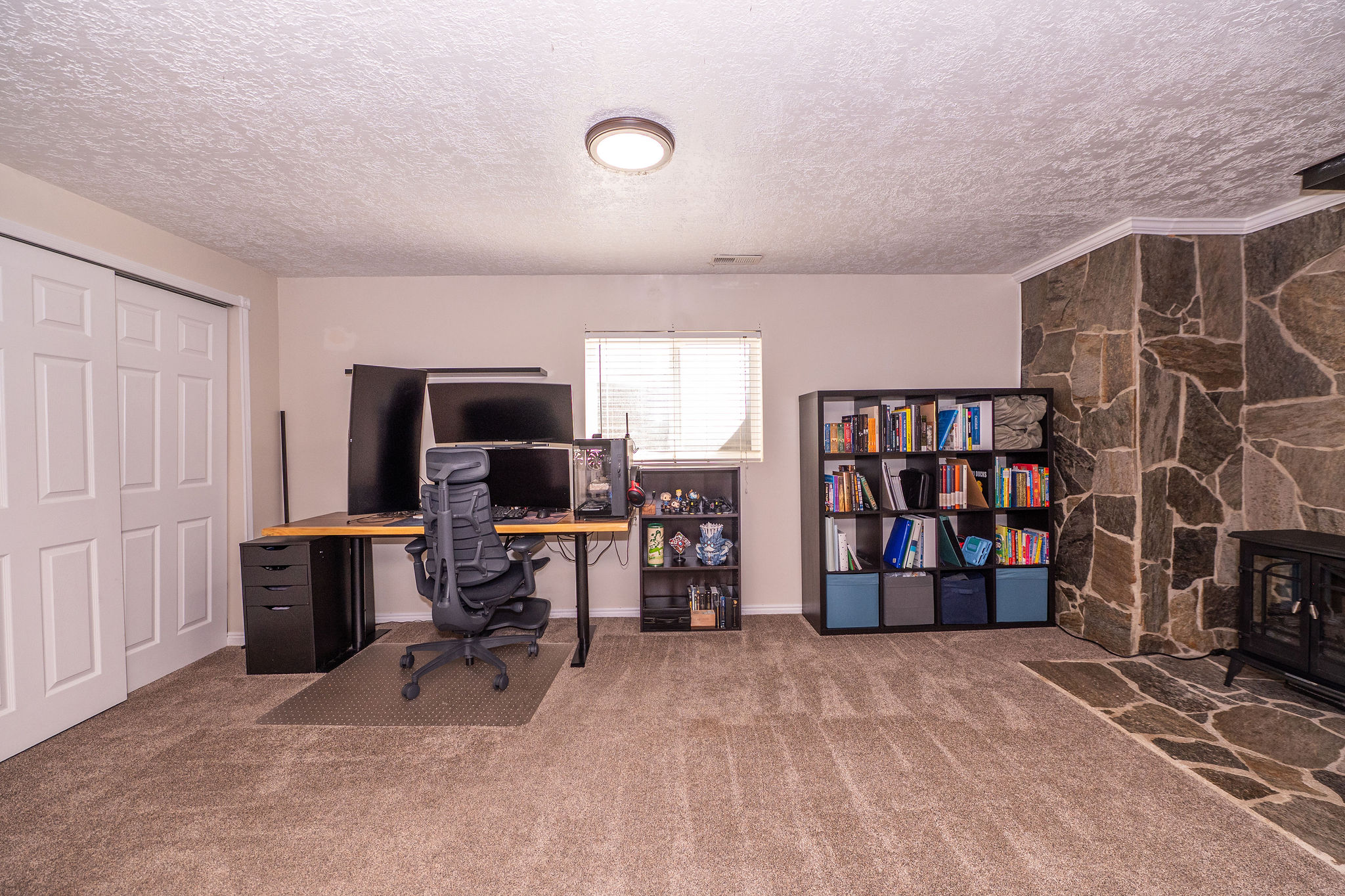 Versatile room featuring a stone-clad wall, large window with blinds, light-colored walls, and textured ceiling