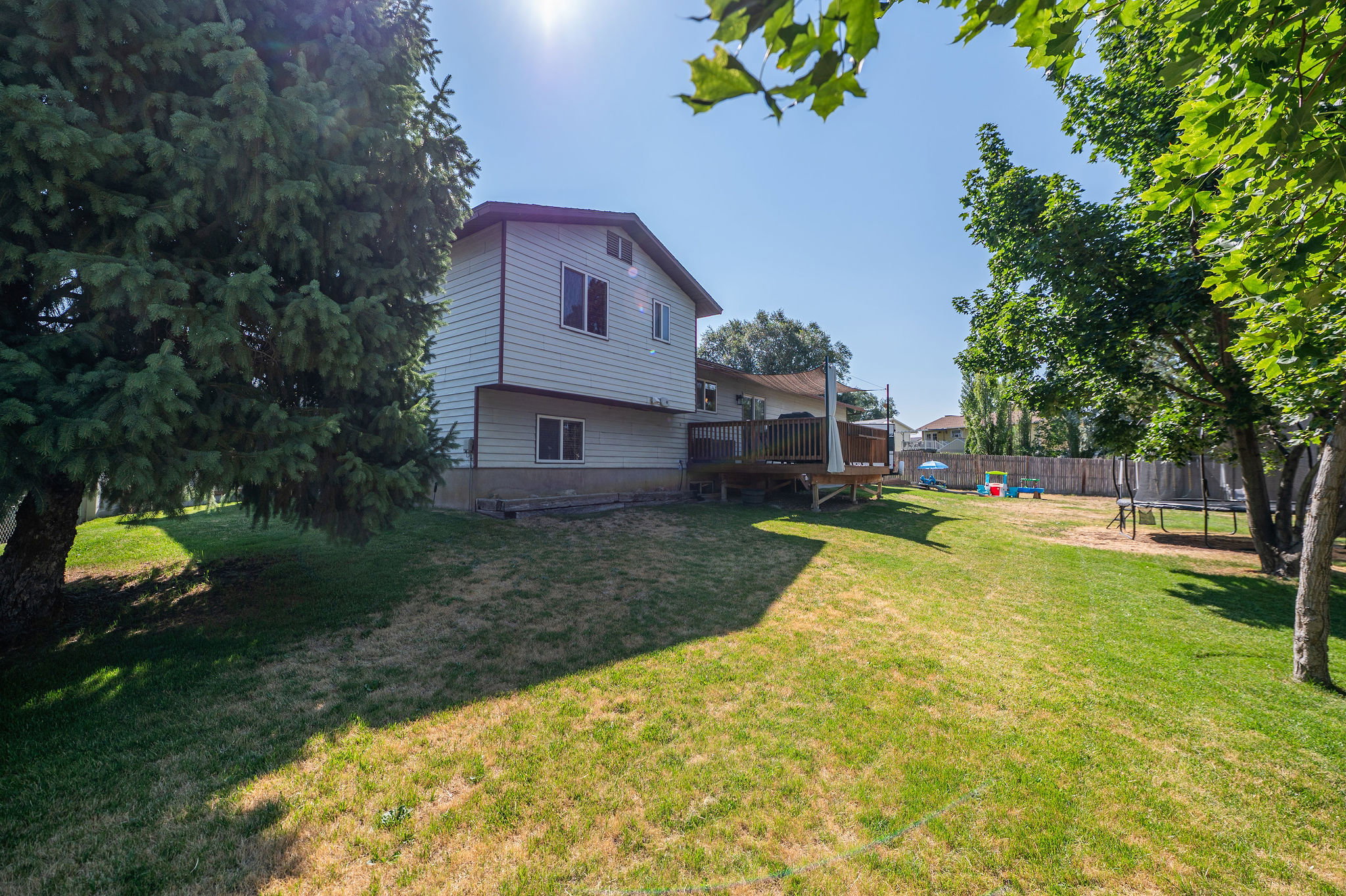 Spacious backyard featuring a multi-level deck, mature trees, and a wooden privacy fence