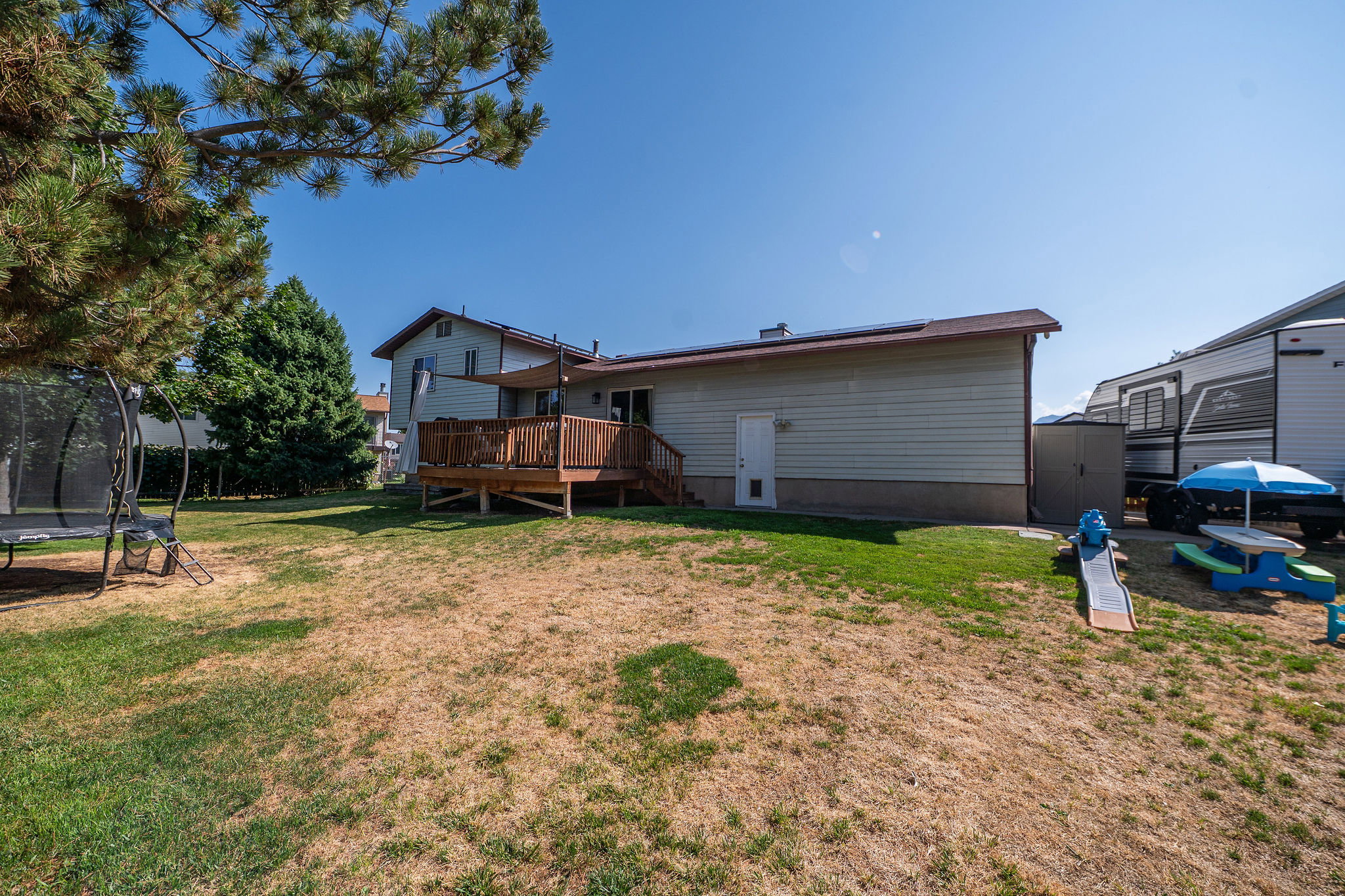 Spacious backyard with a raised wood deck, mature trees, and a sun shade