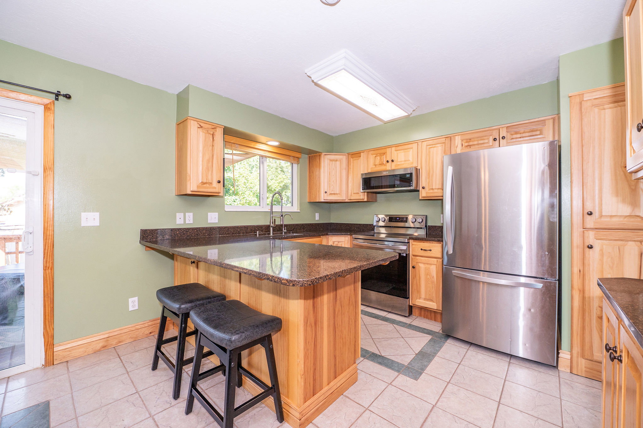 Kitchen featuring light wood cabinetry, stainless steel appliances, granite countertops, and tile flooring