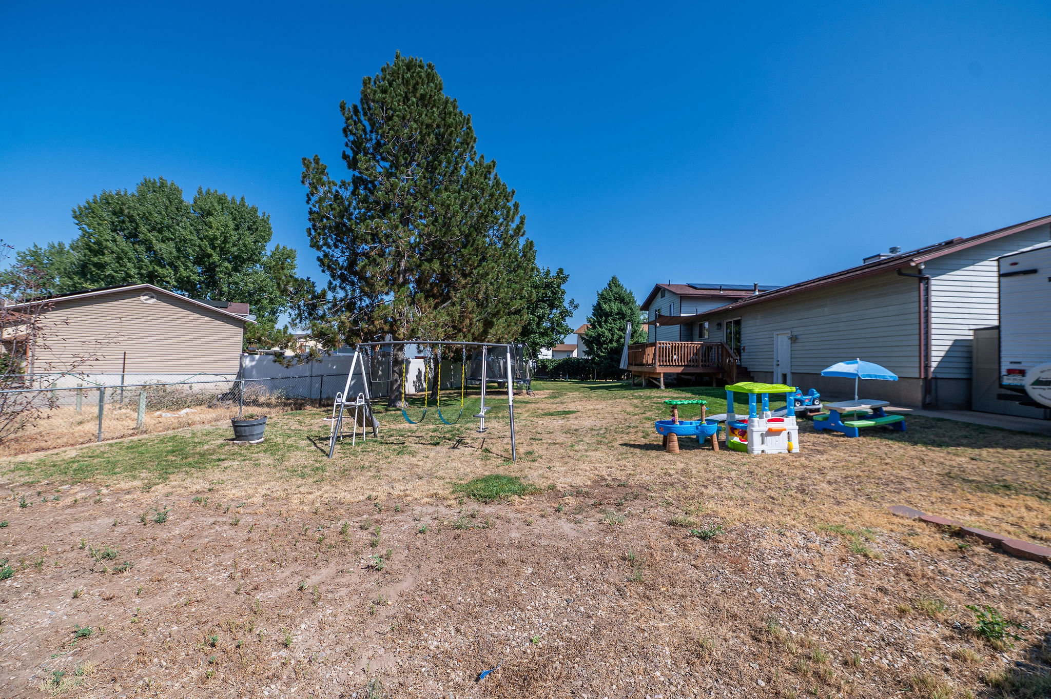 Spacious backyard featuring a chain link fence, mature trees, and a raised wood deck