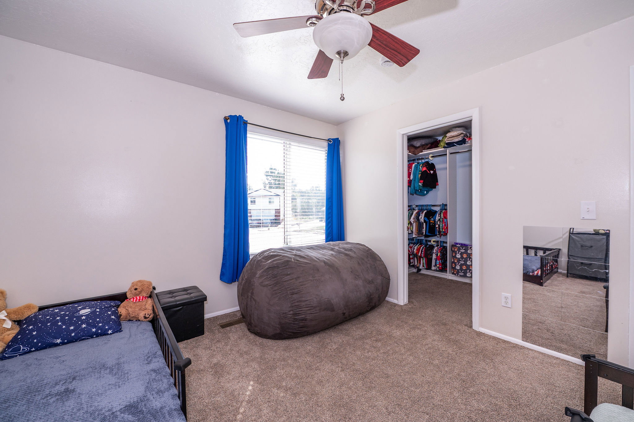 Carpeted room featuring a ceiling fan with integrated lighting, a sliding window with blinds, and a closet with bi-fold doors