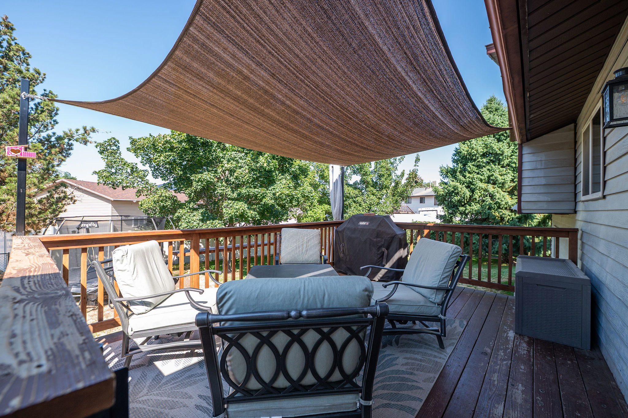 Spacious exterior deck featuring a dark wood finish, a fabric shade canopy, and a wood railing